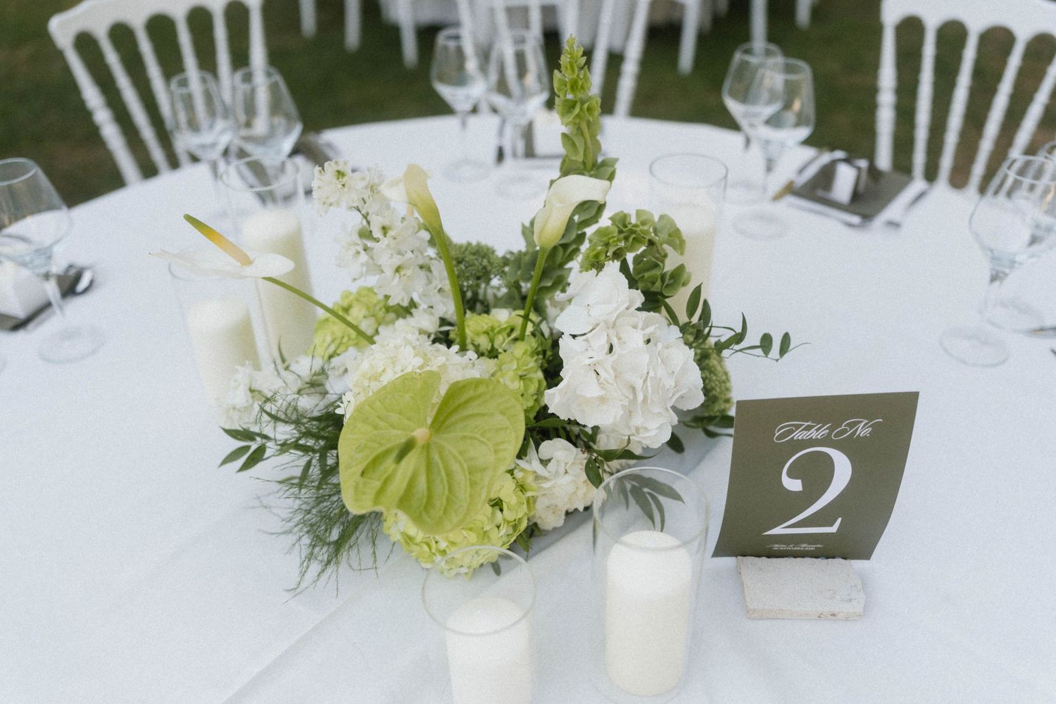 Elegant wedding table centerpiece with white hydrangeas, green anthurium flowers, candles, and a table number 2 sign.