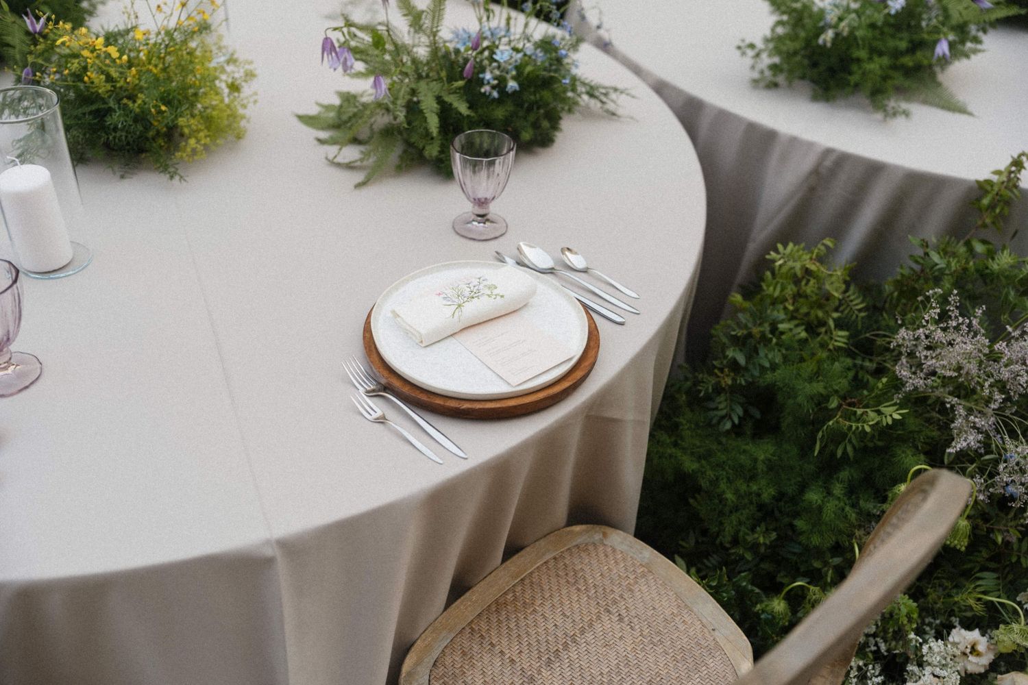 Elegant wedding reception table setting with greenery centerpiece, wooden charger plates, and neutral linen.
