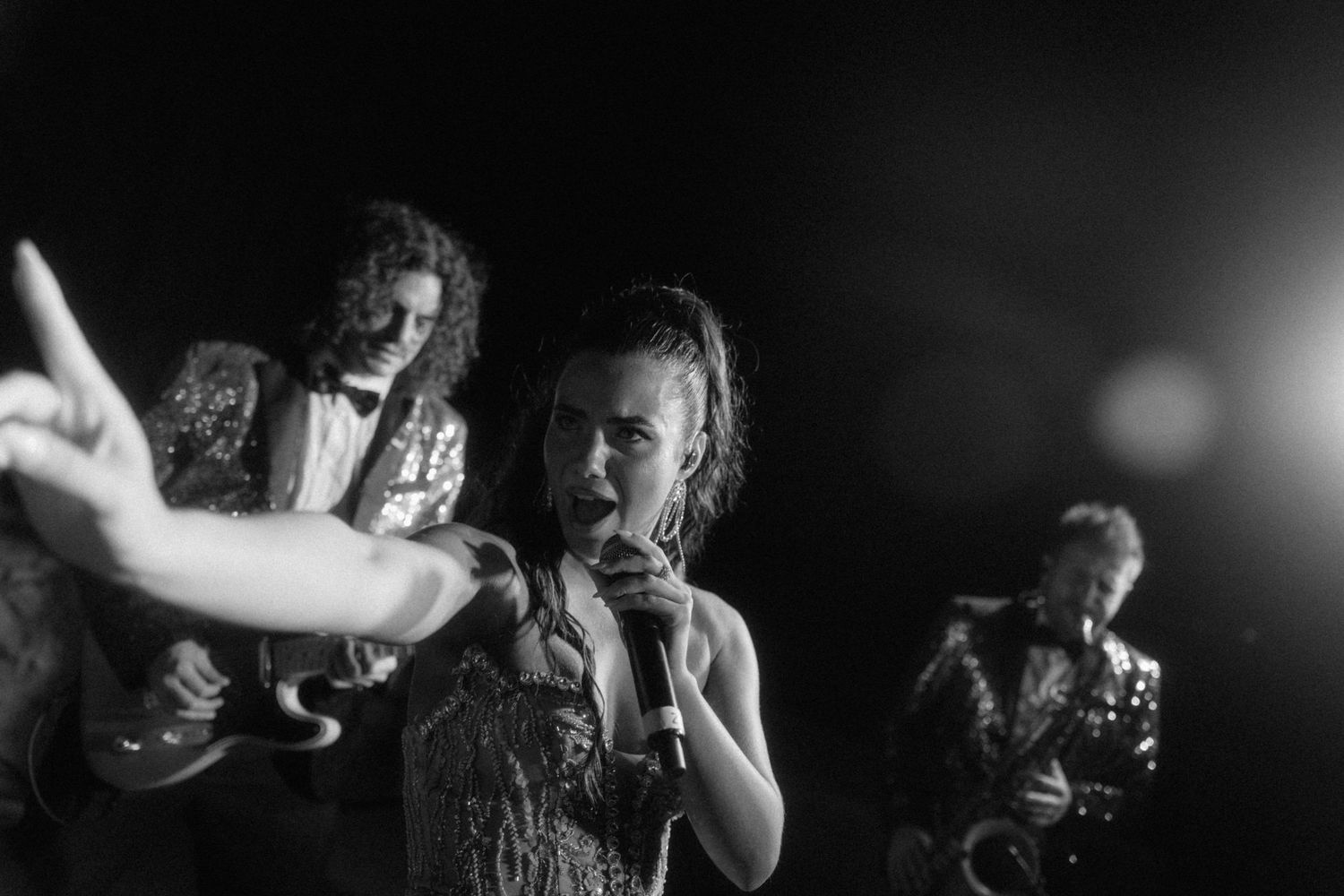 Black and white photo of energetic female singer performing with full band at wedding reception.