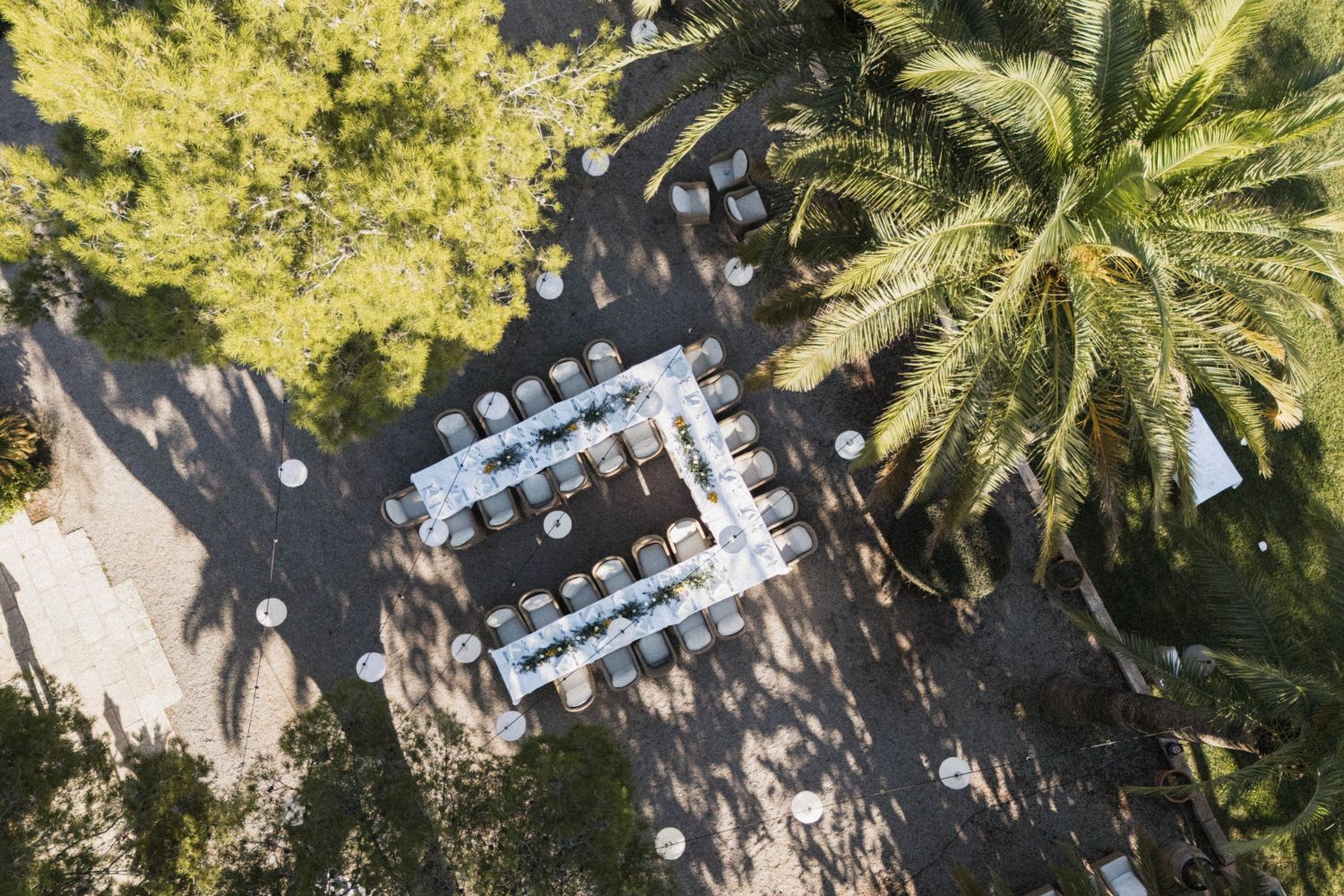 Aerial view of outdoor wedding reception tables arranged in U-shape among lush green trees.