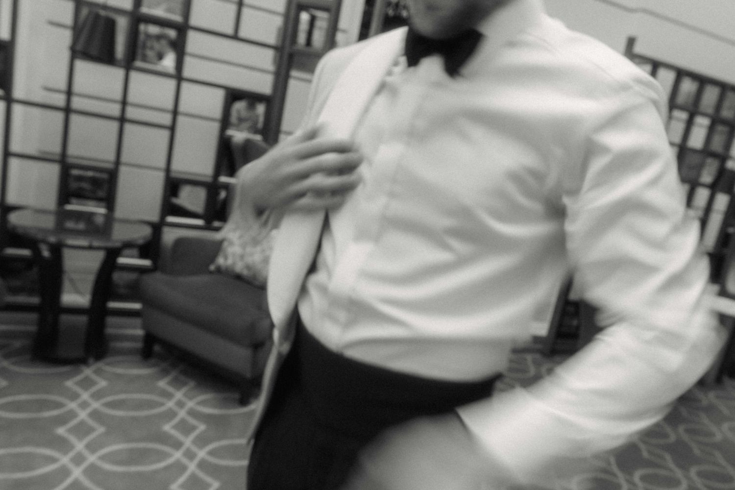 Man in white dress shirt and black bow tie adjusting collar in black and white photo.
