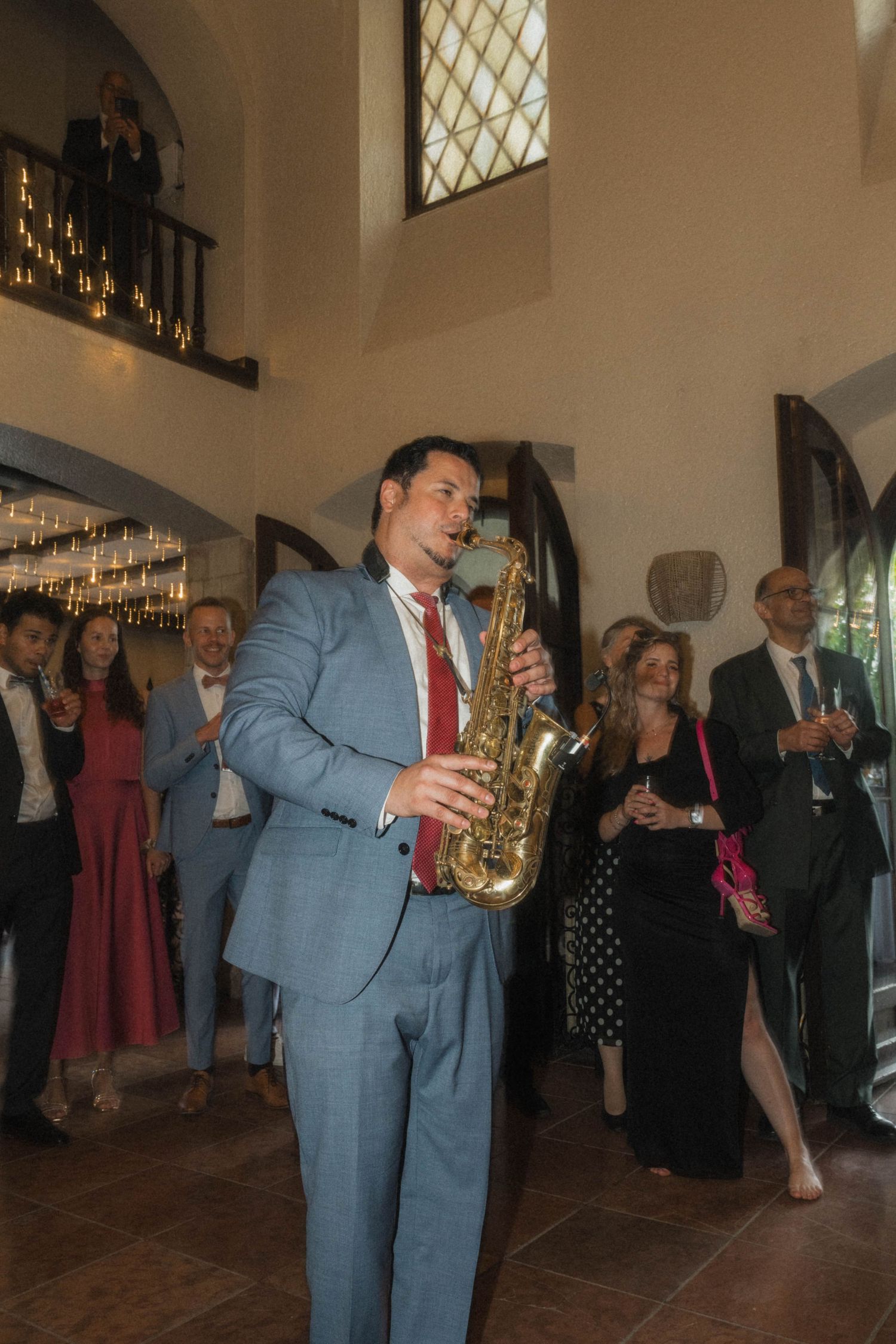 A man in a blue suit plays saxophone at an elegant wedding reception while guests watch and celebrate.