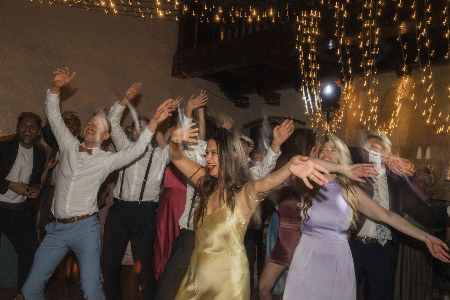 Wedding guests dancing energetically under fairy lights at a lively reception party.