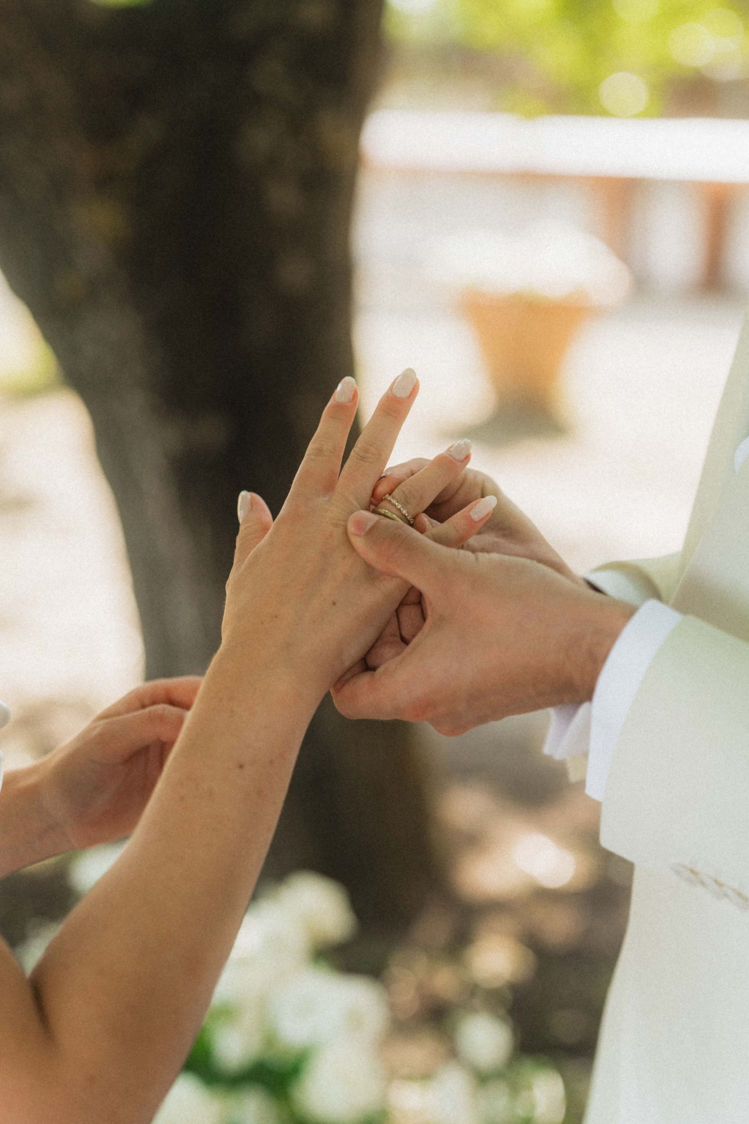 Close-up of groom placing wedding ring on bride's finger during outdoor ceremony with soft natural lighting.