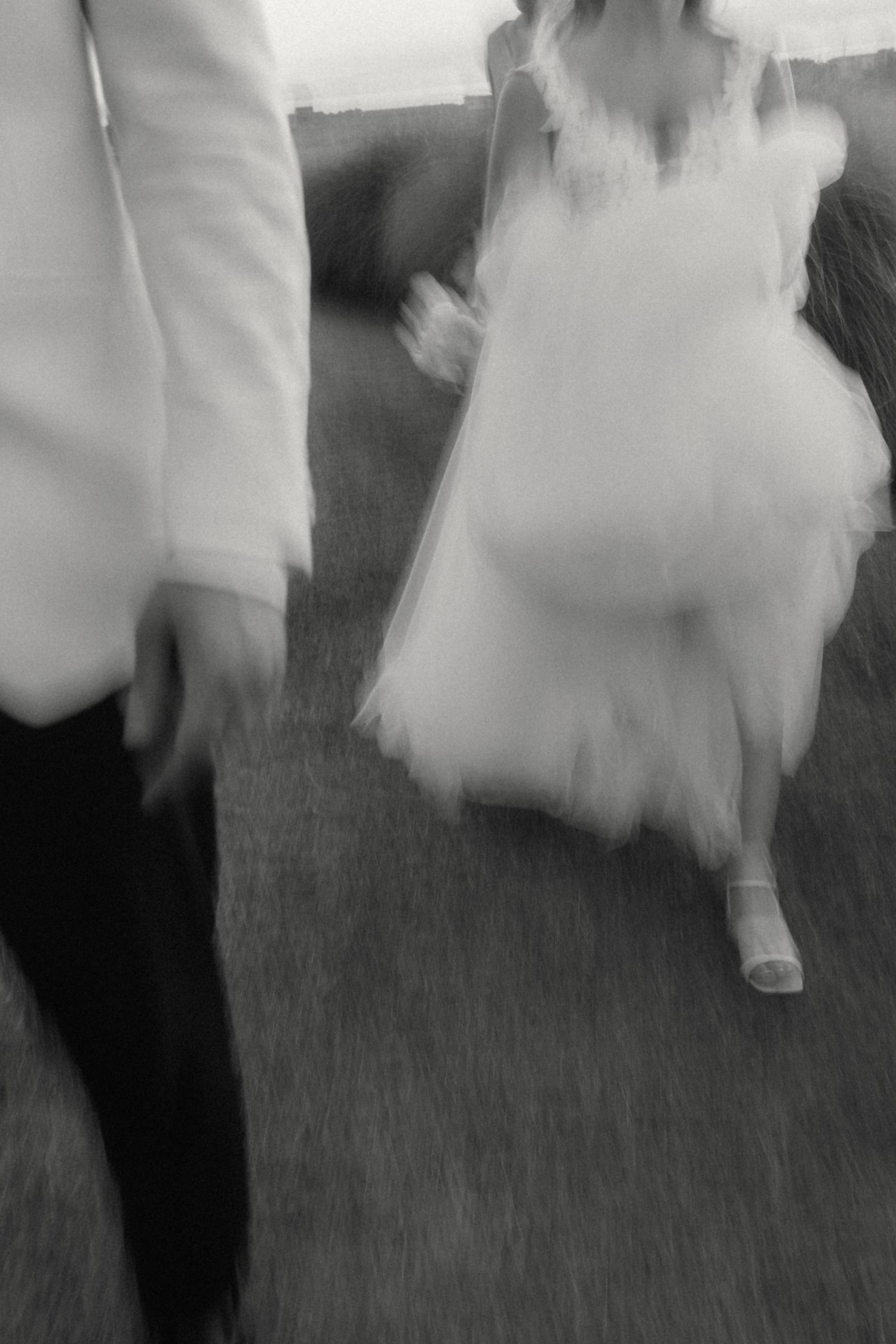 Blurred black and white artistic photo of bride in tulle gown and groom walking together outdoors.