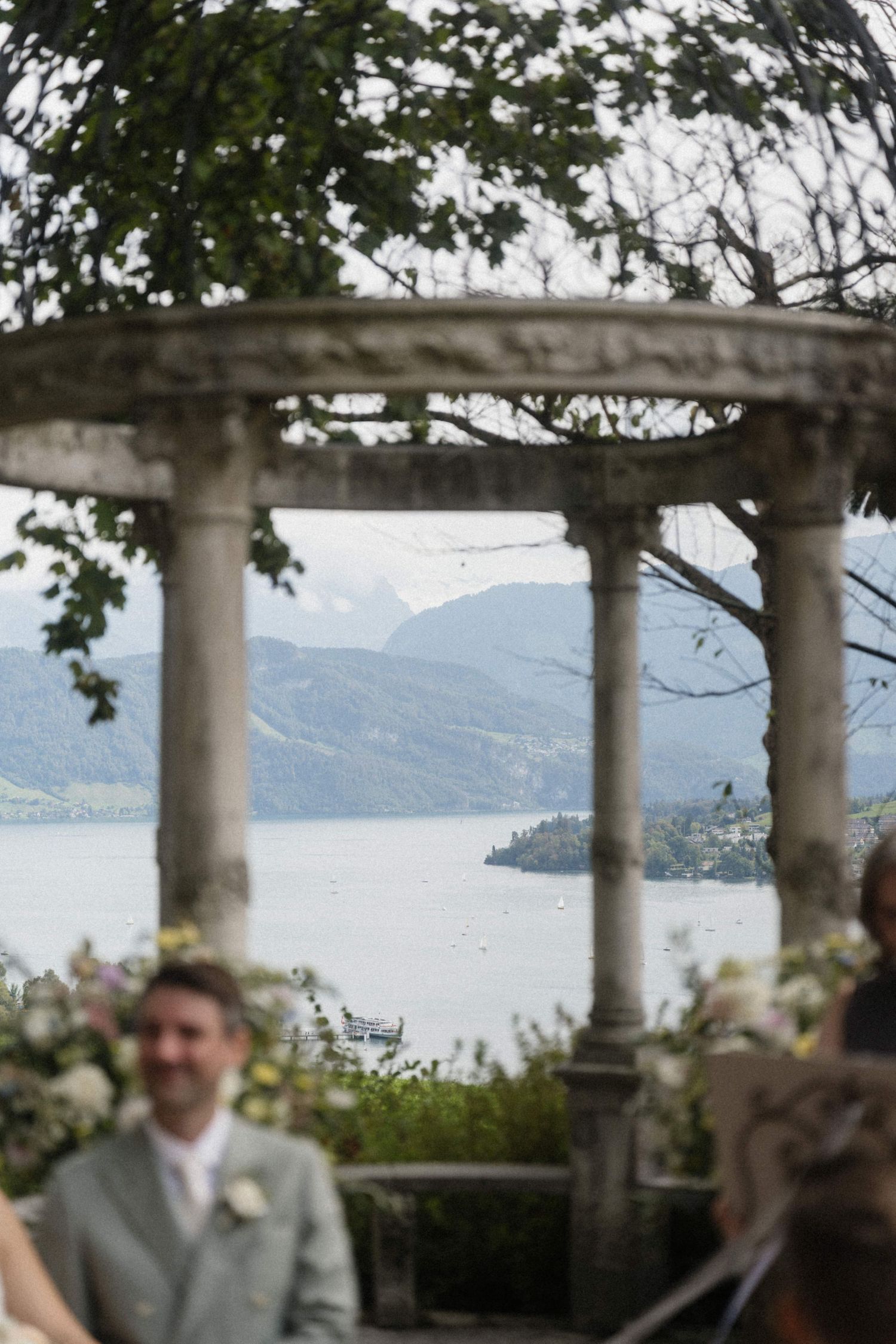 Stone gazebo with classical columns framing a stunning lake and mountain view at a wedding ceremony.