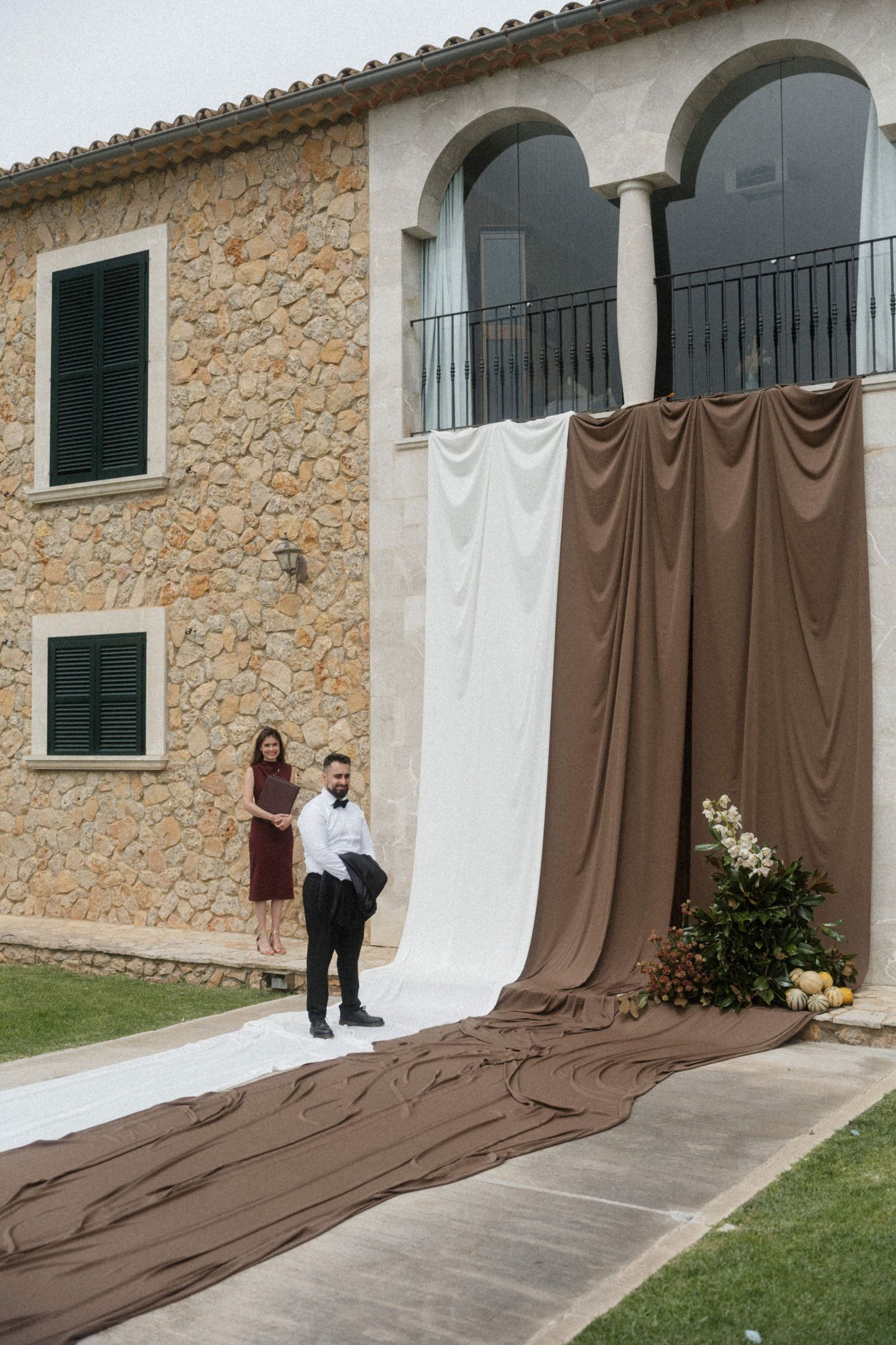 Elegant wedding ceremony setup with brown and white draped fabric against a rustic stone villa facade.