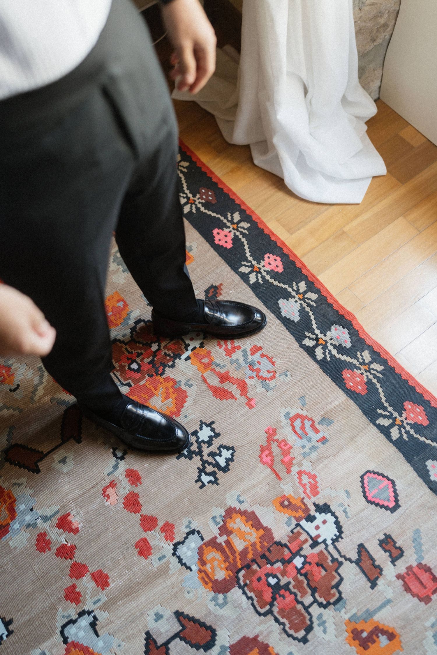 Close-up of groom's polished black dress shoes on a colorful floral patterned wedding rug.