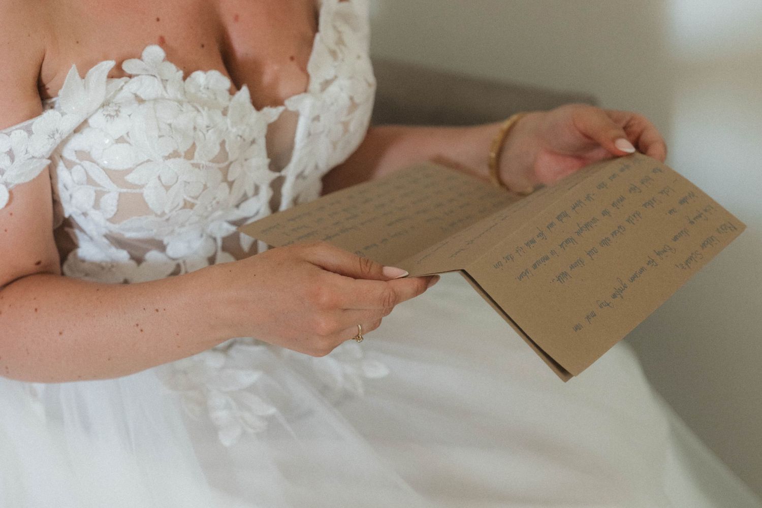 Bride in white lace wedding dress reading a handwritten letter on her wedding day.
