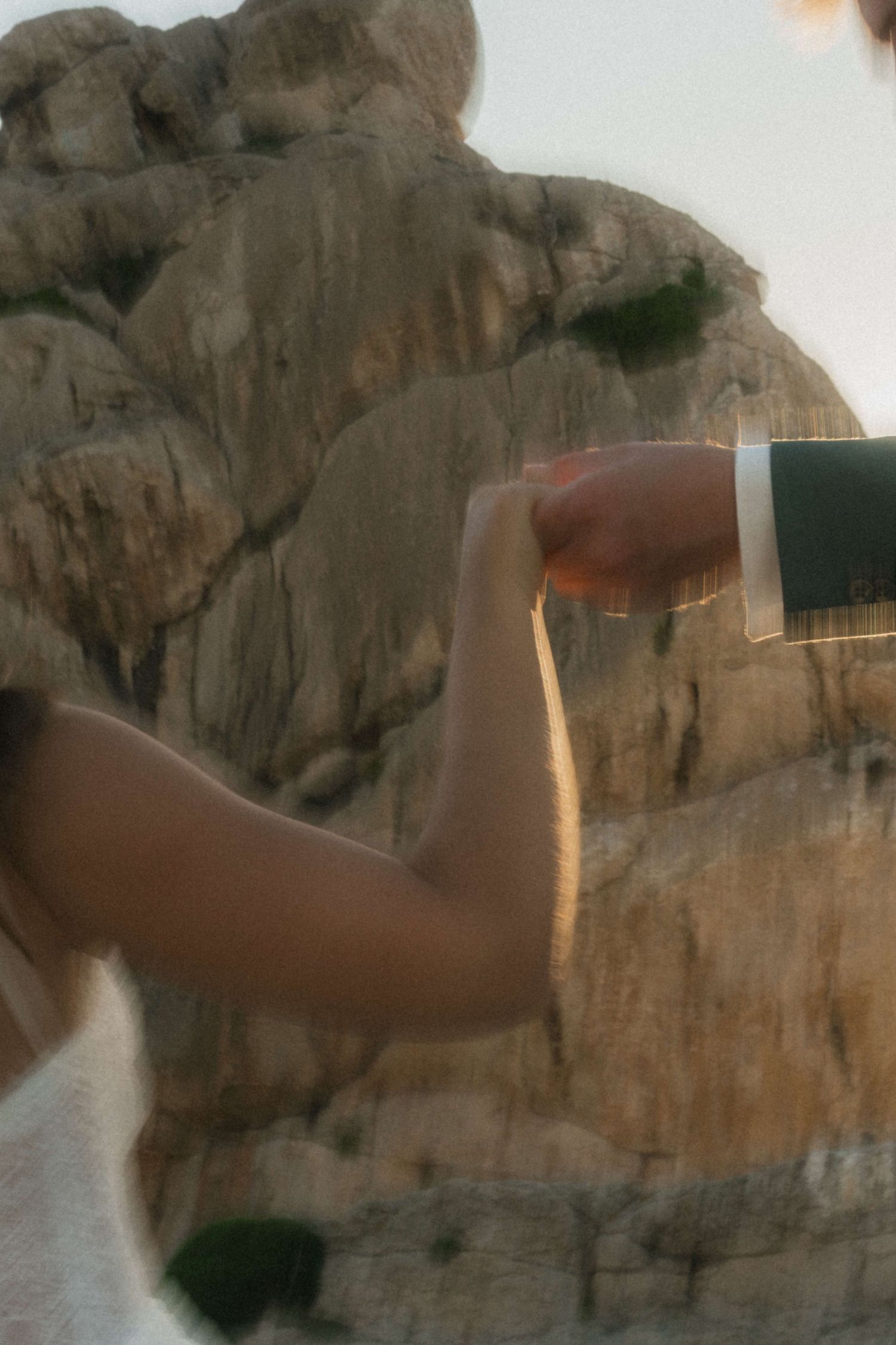Bride and groom holding hands near rocky cliffs during golden hour outdoor wedding ceremony.
