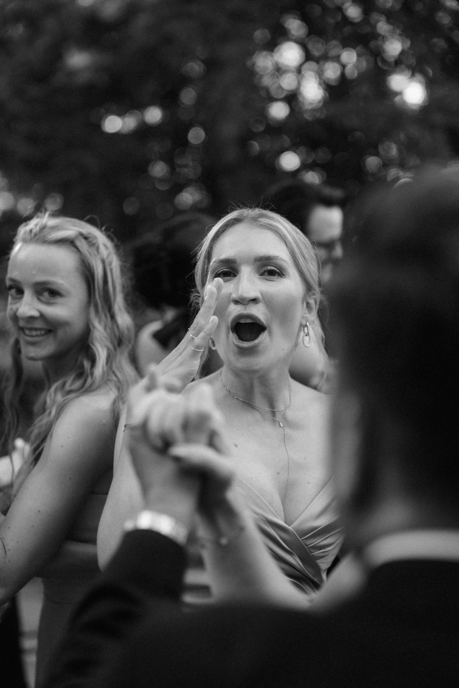 Black and white candid photo of excited wedding guest reacting with open mouth surprise at reception.