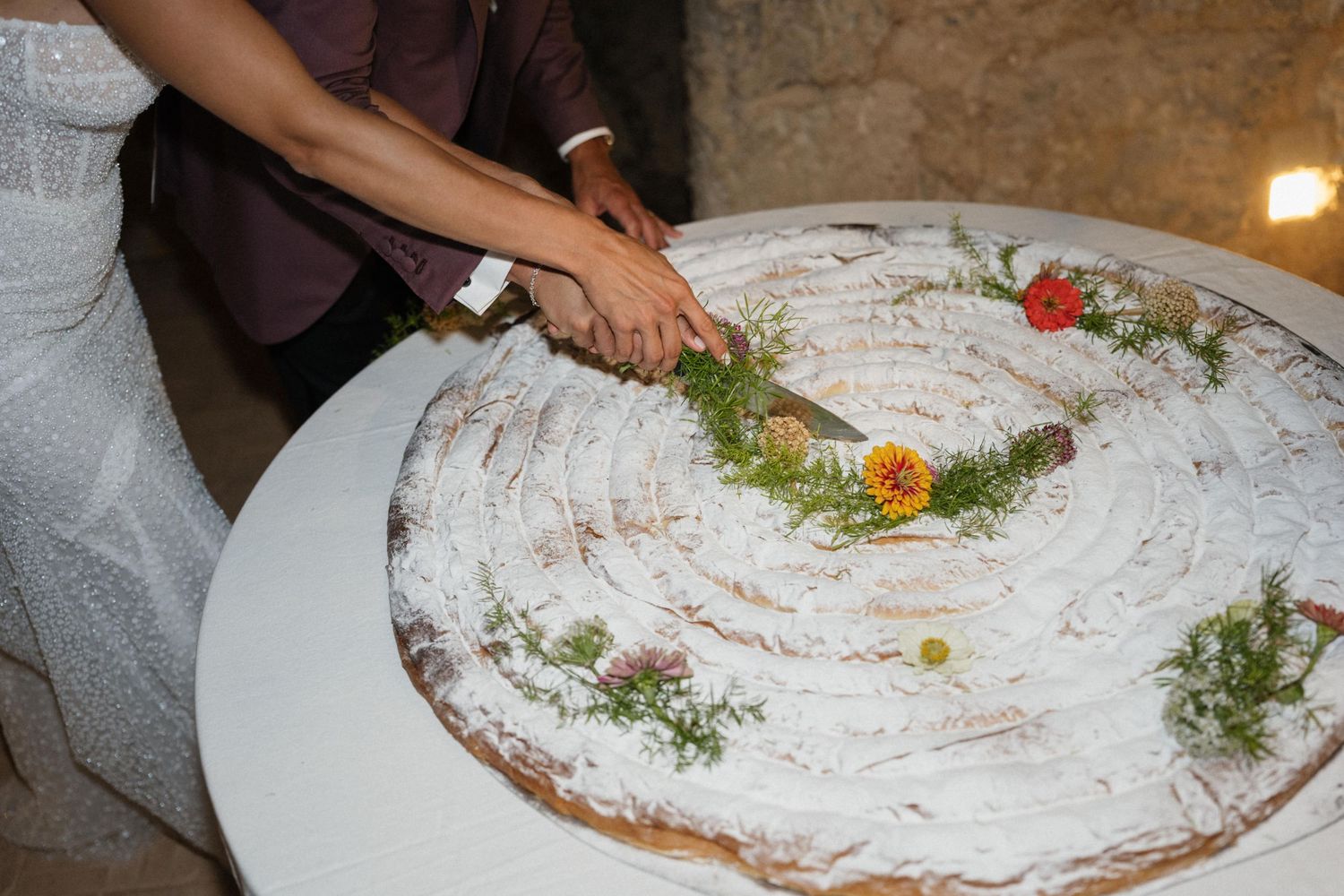 Bride and groom cut a large wedding cake decorated with fresh flowers and herbs together.