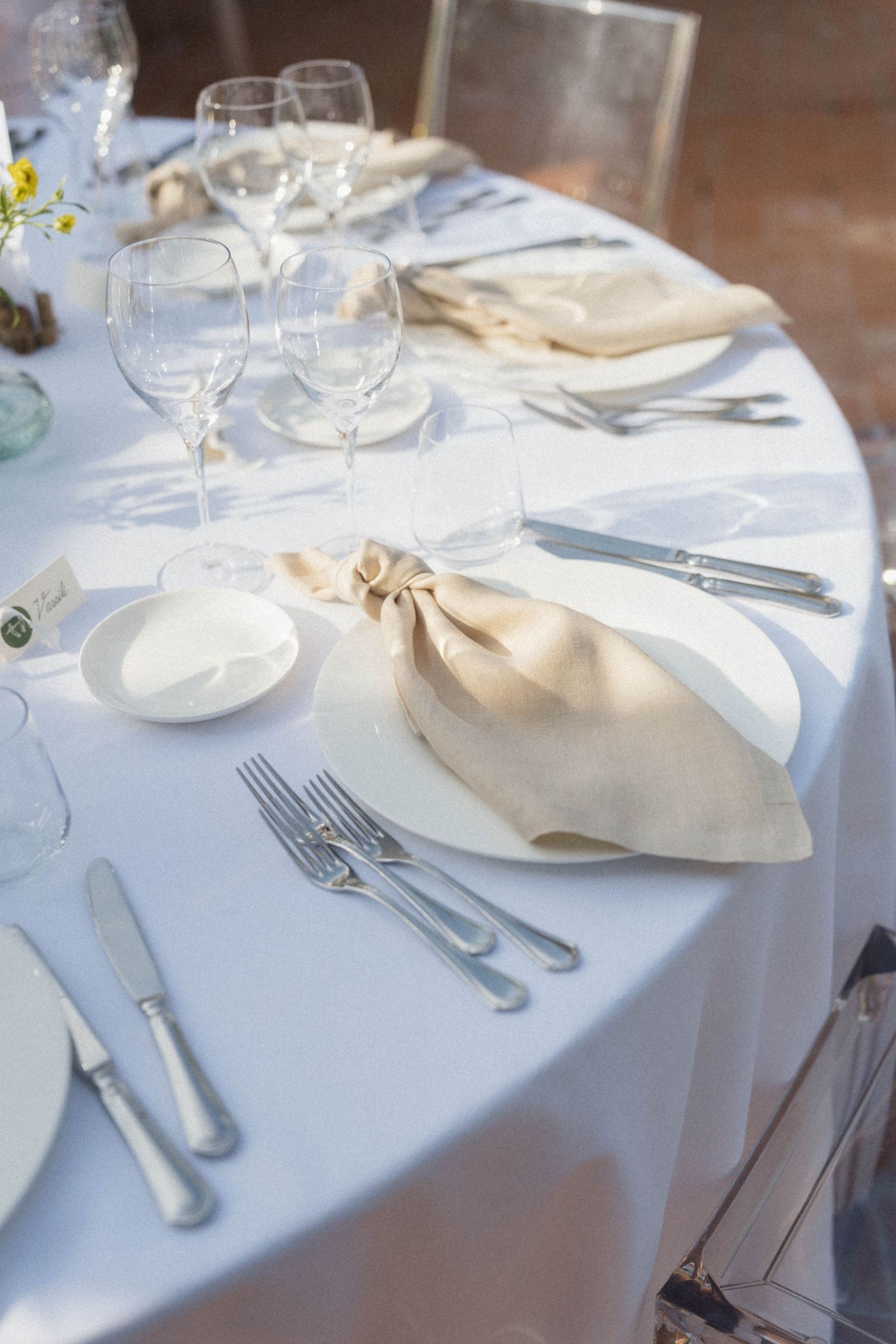 Elegant white round table setting with linen napkins, wine glasses, and silverware for a formal wedding reception.
