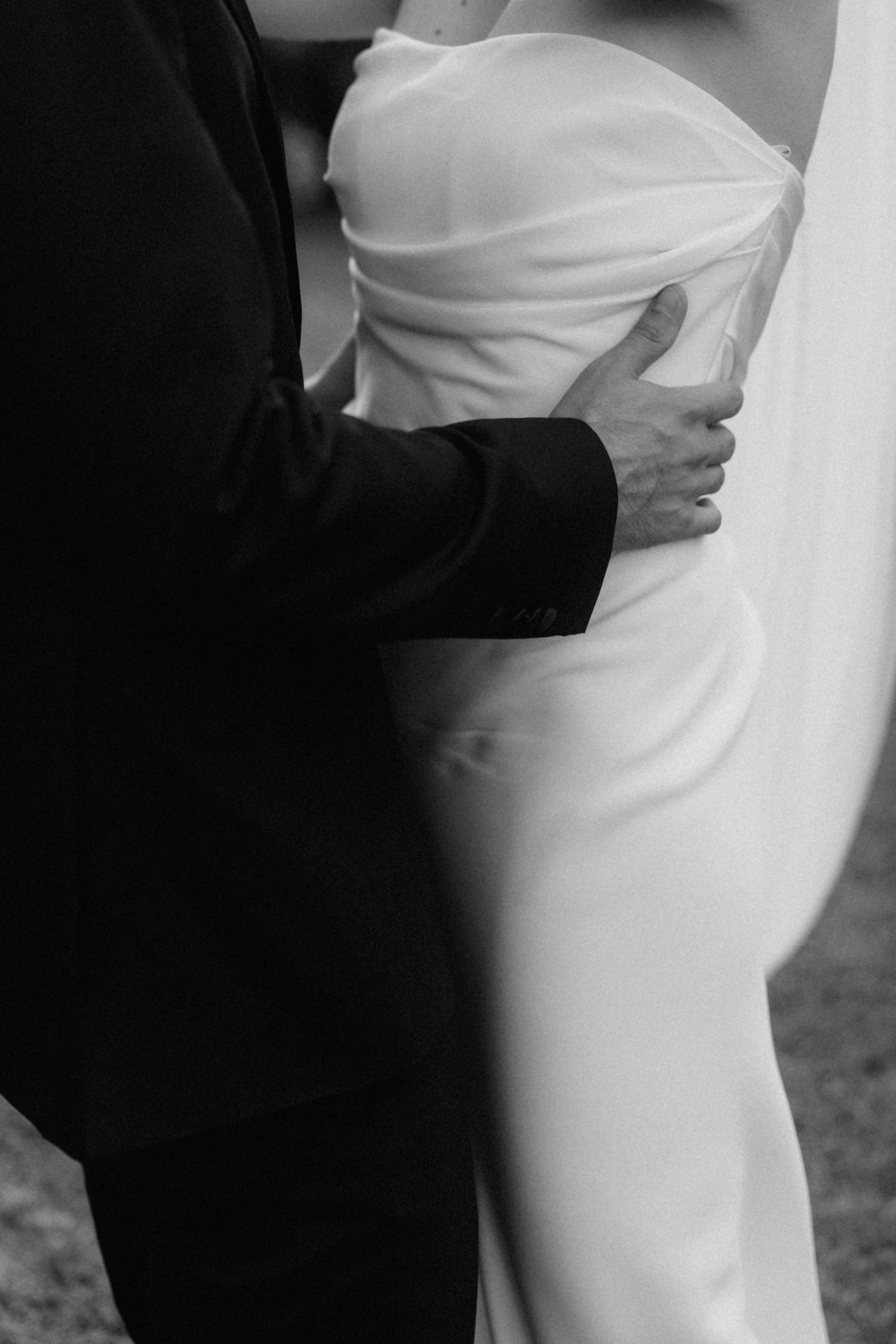 Black and white close-up of groom tenderly placing hand on brides waist in elegant strapless wedding gown.