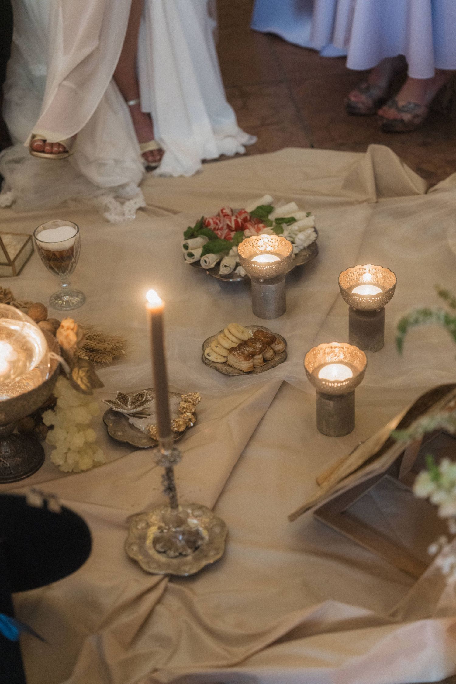 Rustic wedding ceremony table with candles, traditional foods, and decorative items on linen.