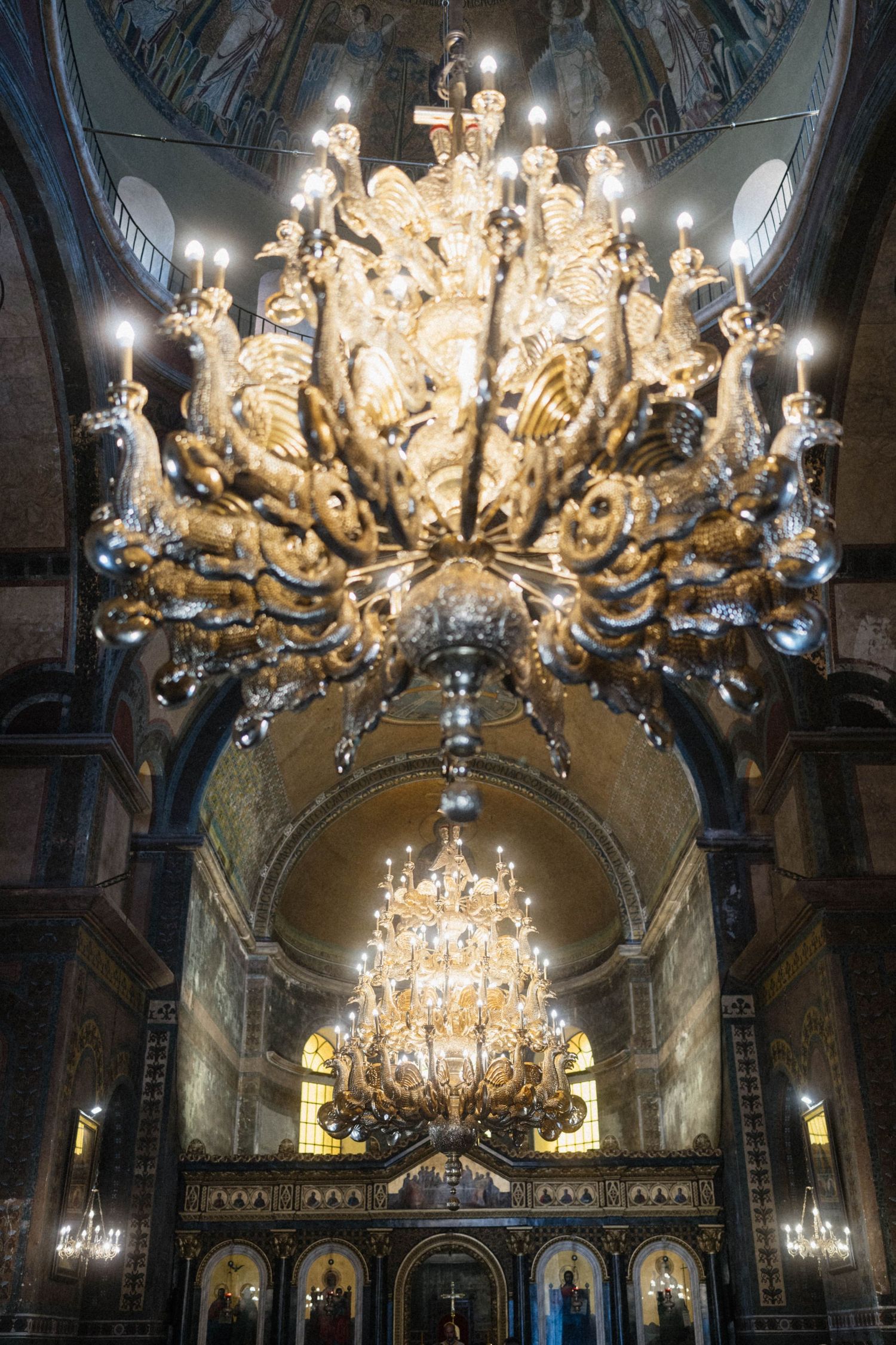 Ornate golden chandelier with candles illuminating the interior of an Orthodox cathedral with mosaic dome.