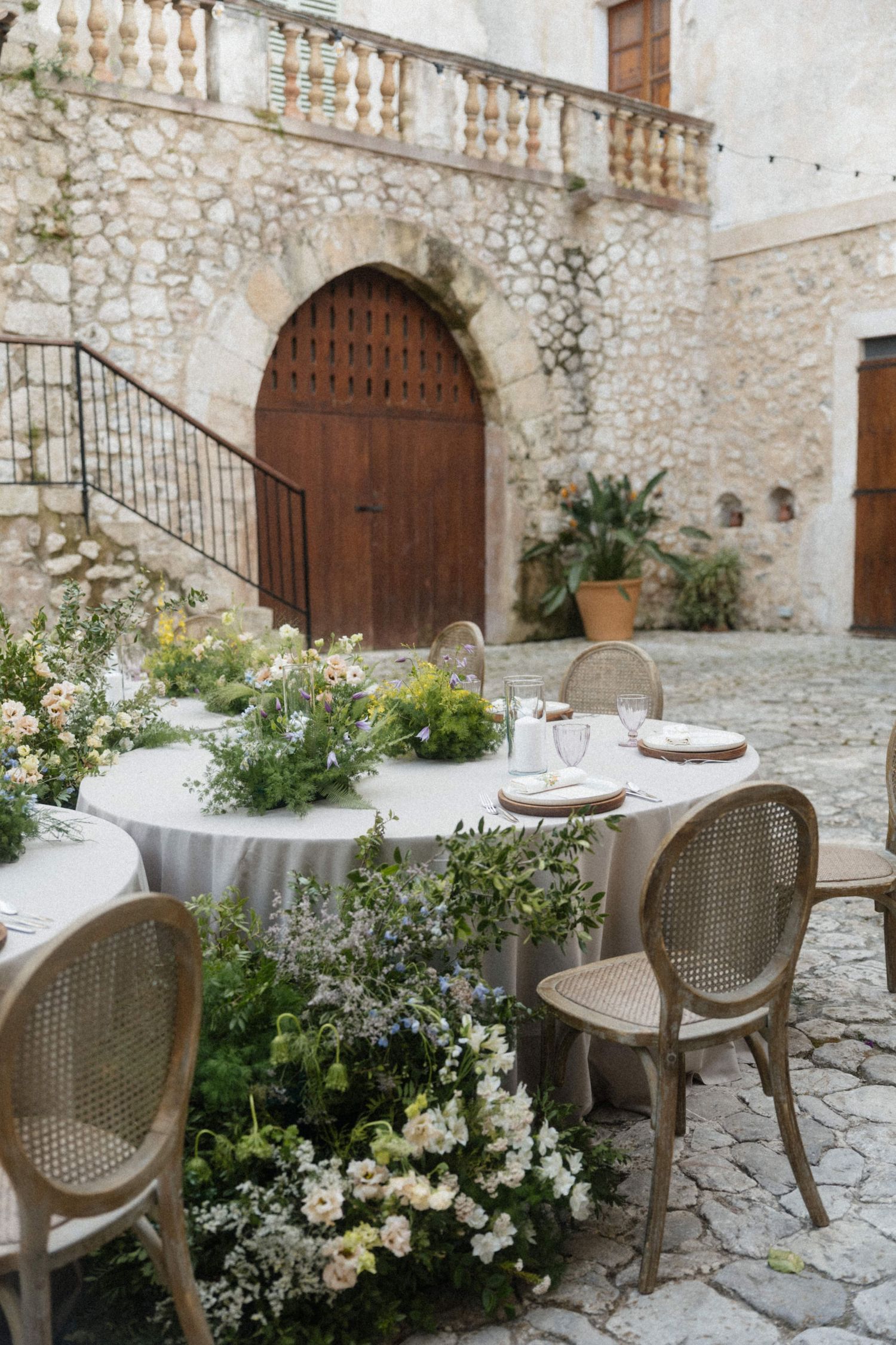 Rustic outdoor wedding reception setup in historic stone courtyard with floral decorations.
