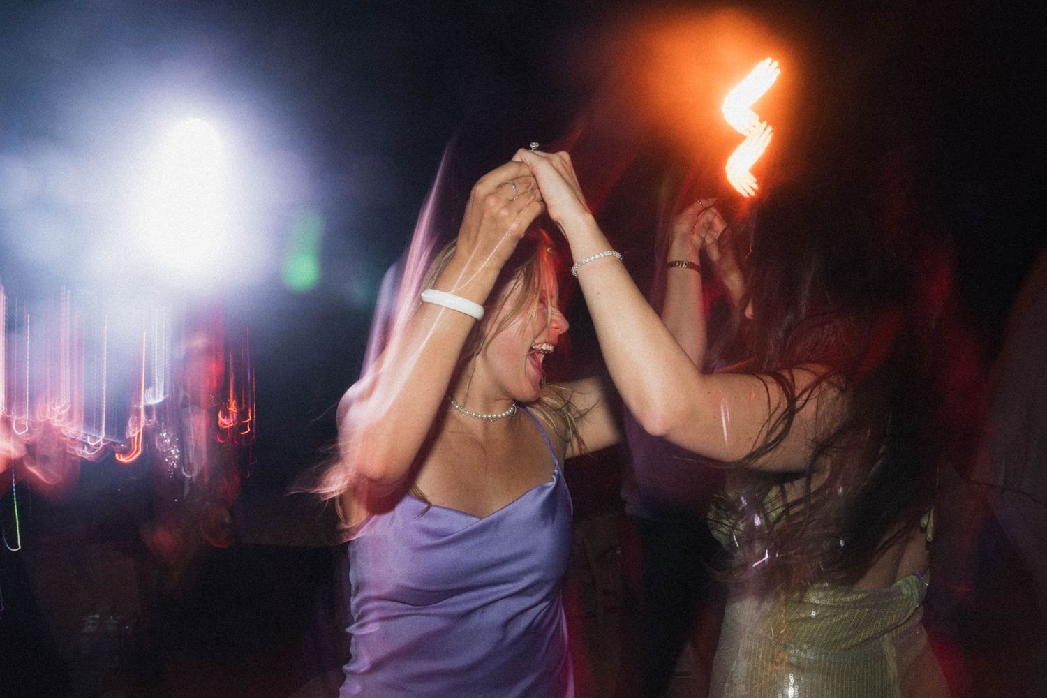 Two women dancing energetically at a nightclub party with colorful stage lighting and smoke.