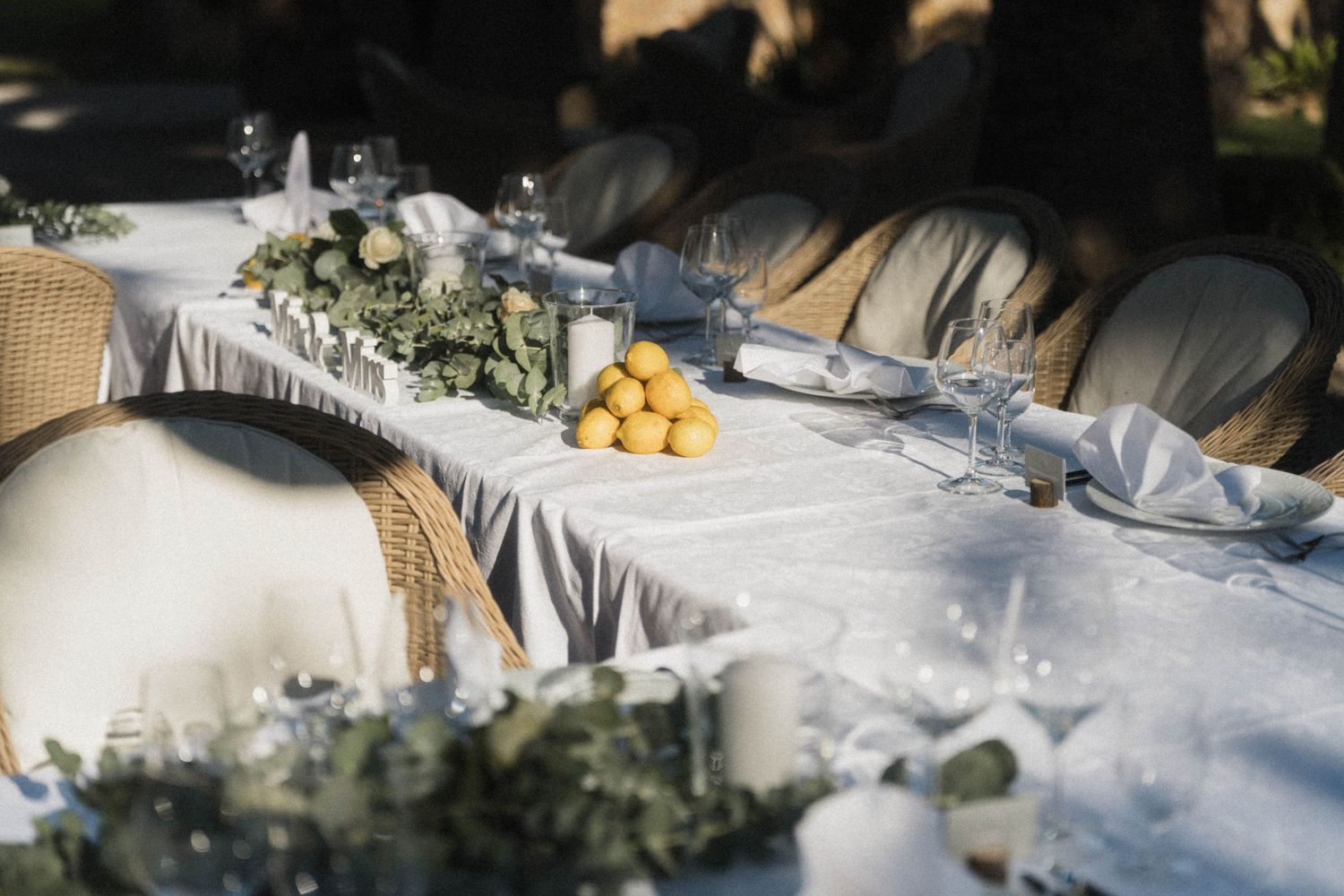 Outdoor wedding reception table with lemons centerpiece, eucalyptus, candles, and white linens.