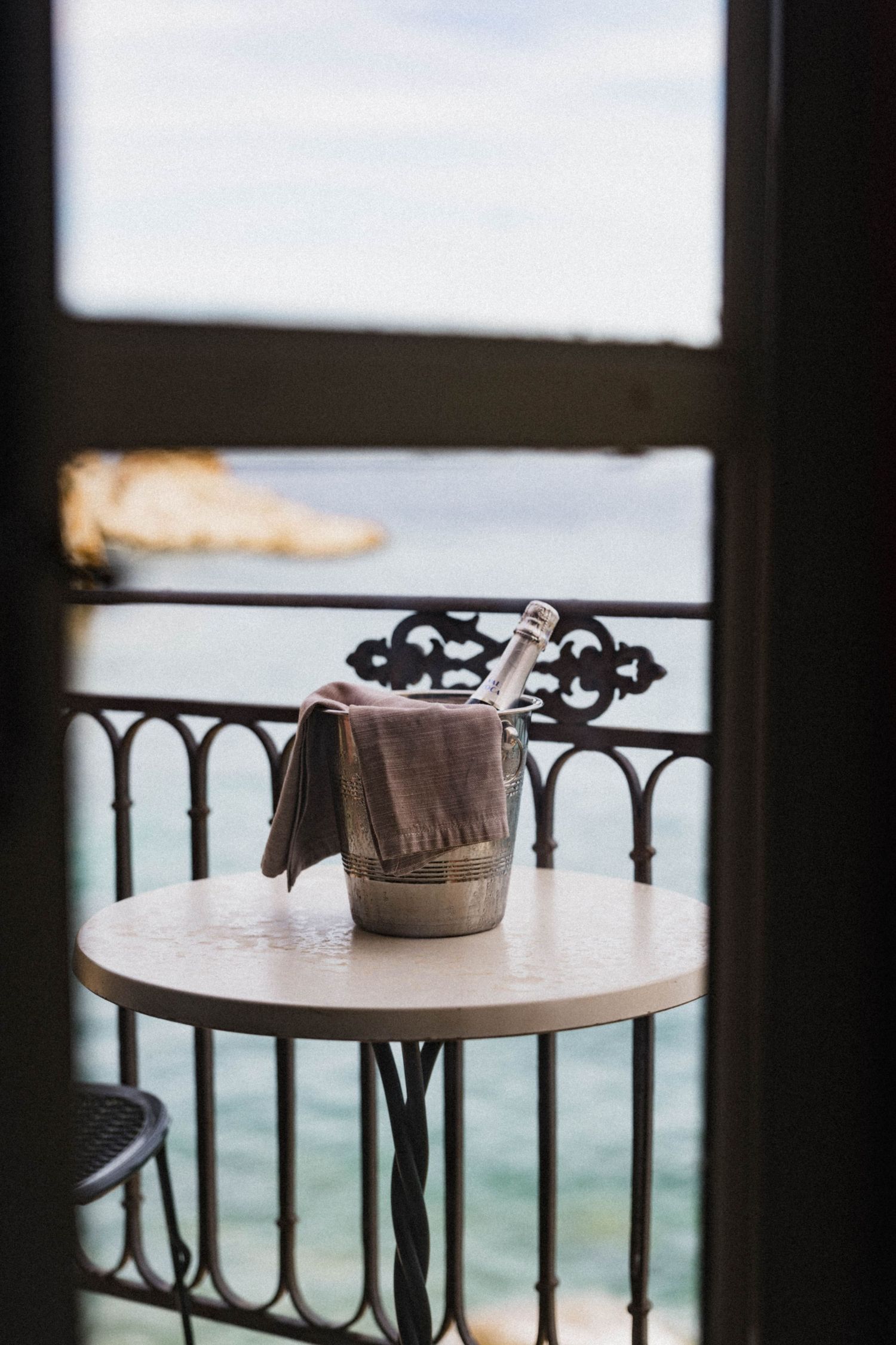 Champagne bottle in ice bucket on balcony table with stunning ocean view at a luxury hotel.