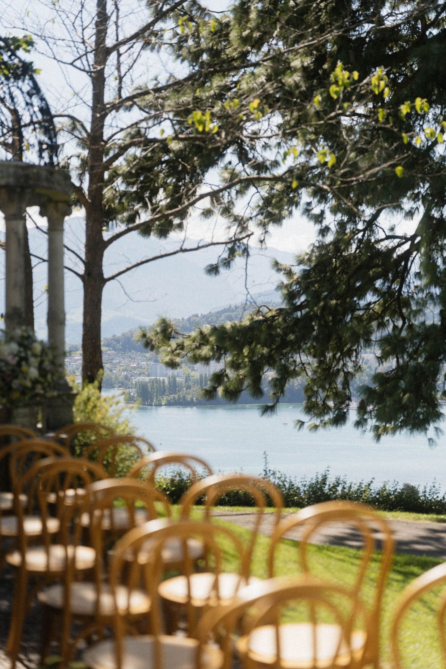 Elegant outdoor wedding ceremony setup with bentwood chairs overlooking a serene lake framed by tall pine trees.