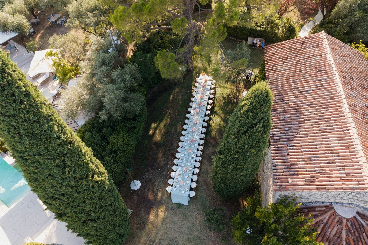 Aerial view of an elegant outdoor wedding reception table set among lush green trees at a Tuscan villa.