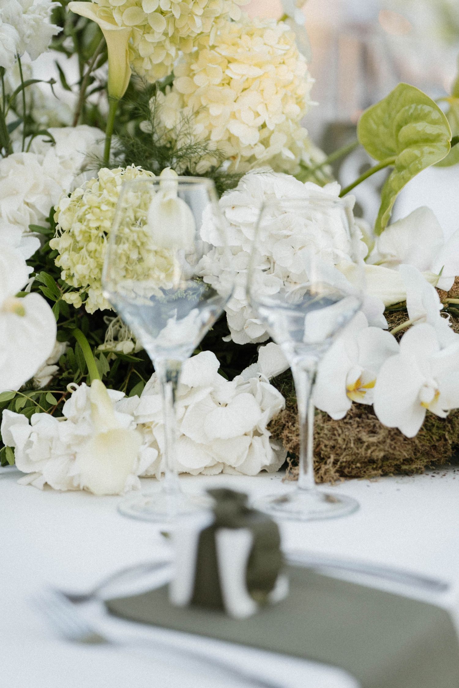 Elegant wedding table setting with white hydrangeas, orchids, and crystal wine glasses on a white tablecloth.