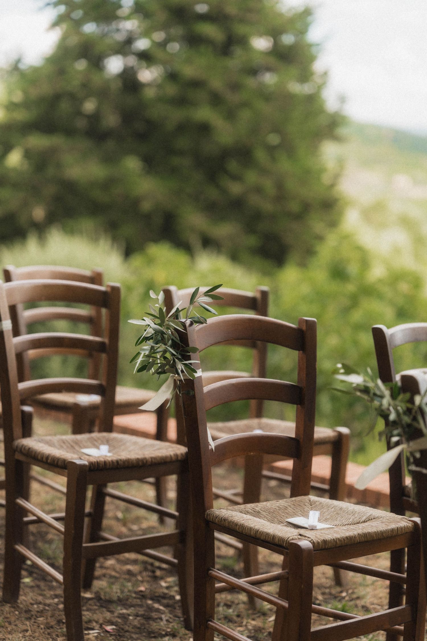 Rustic wooden chairs with woven seats decorated with greenery for an outdoor wedding ceremony.