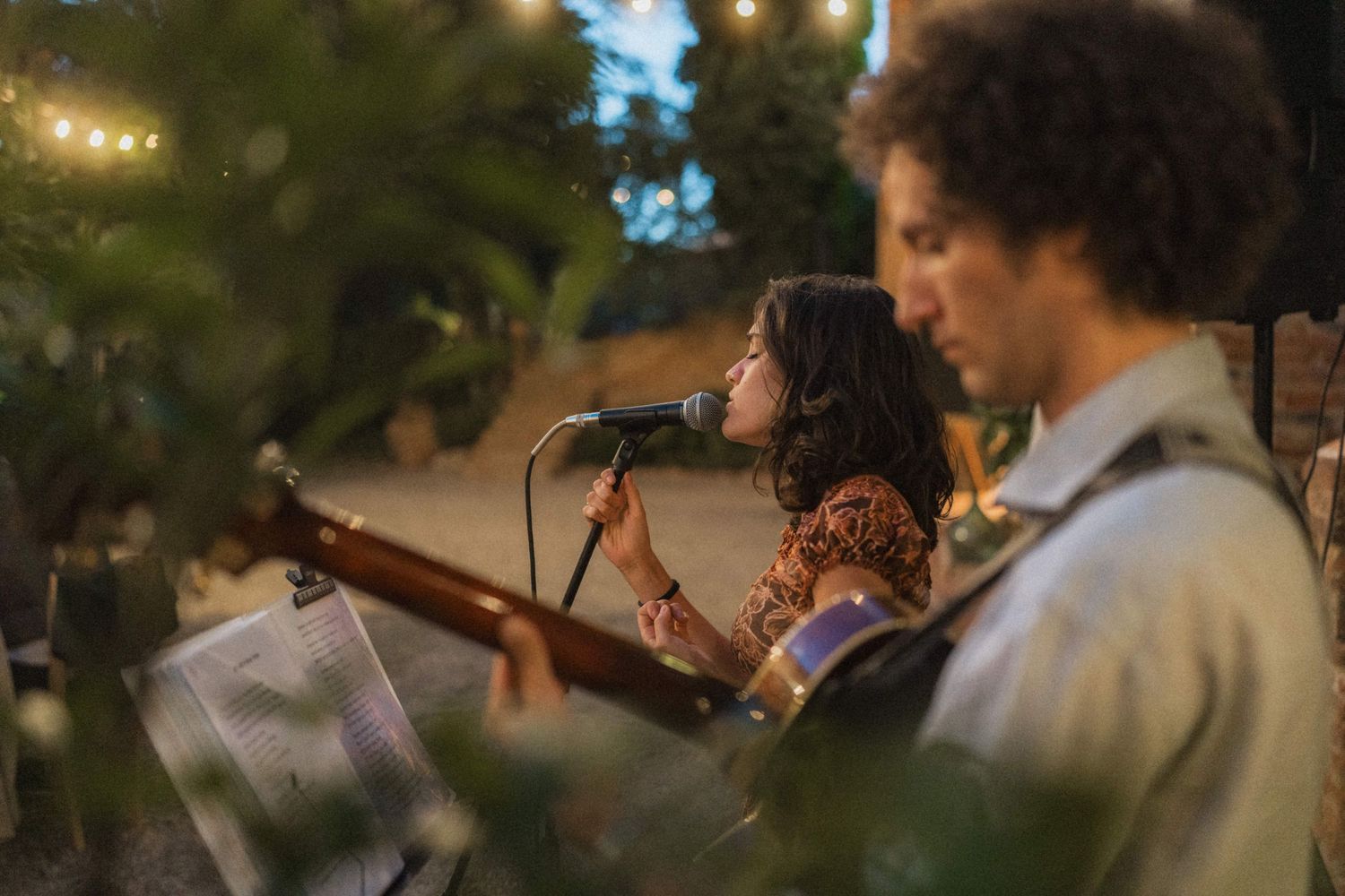 Live band performs at an outdoor evening wedding reception, with a female singer at the microphone.