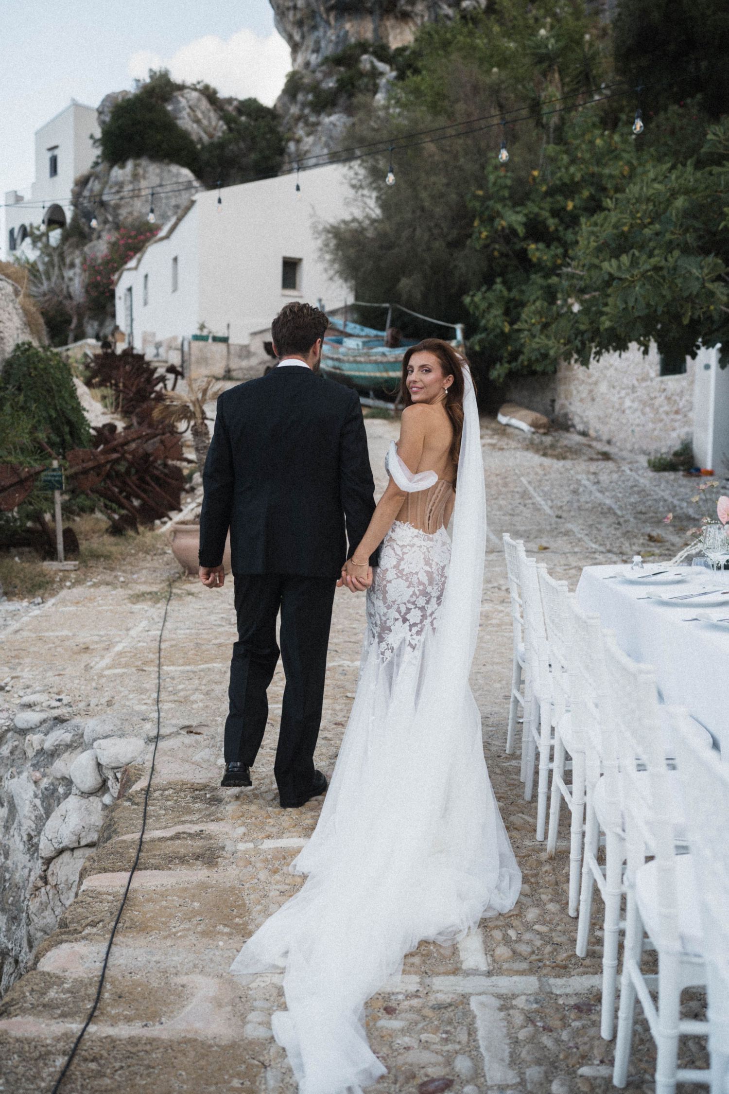 Bride and groom walk hand in hand past reception tables at hillside venue.