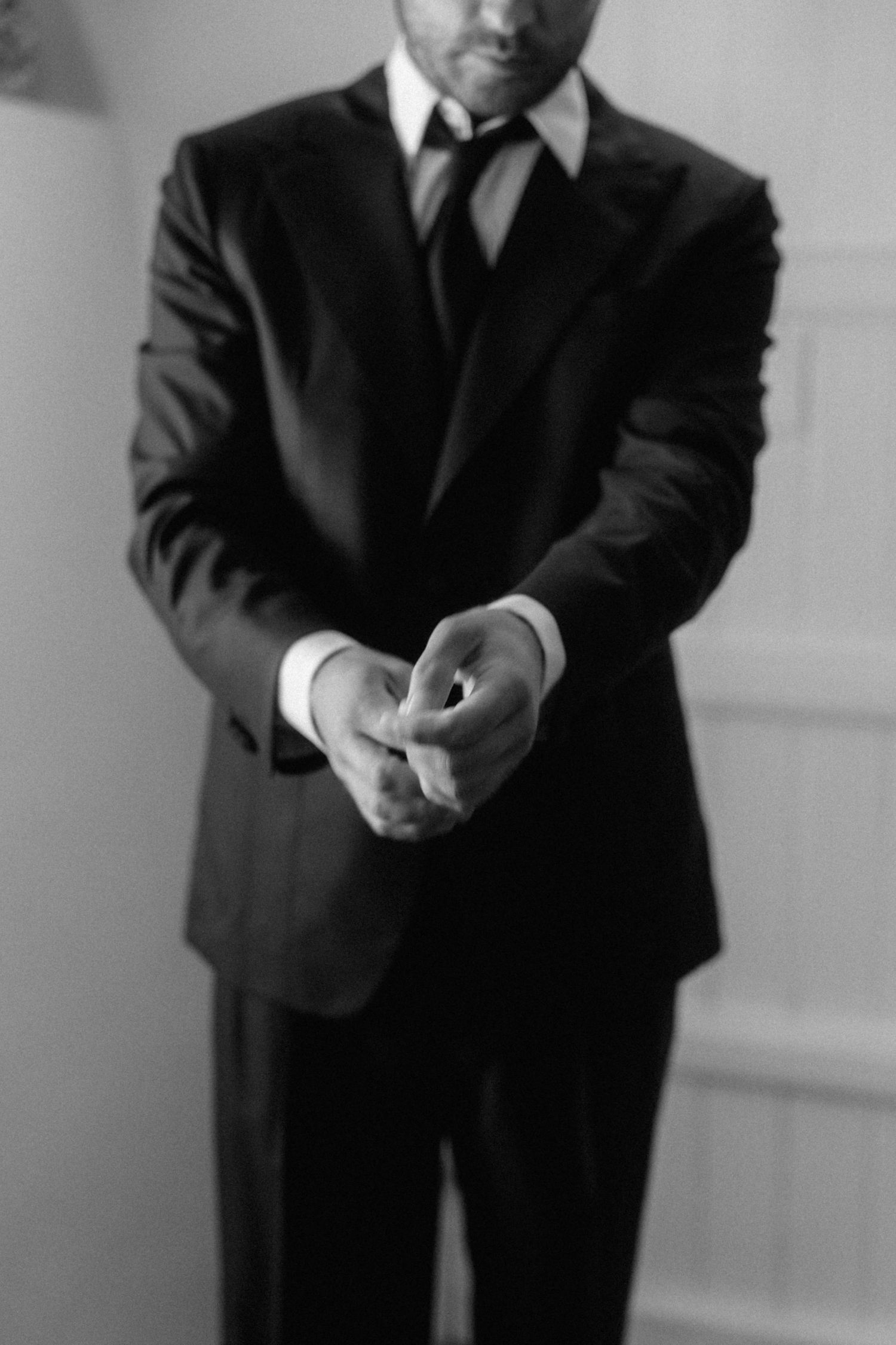 Black and white portrait of groom in dark suit adjusting cufflinks while preparing for his wedding day.