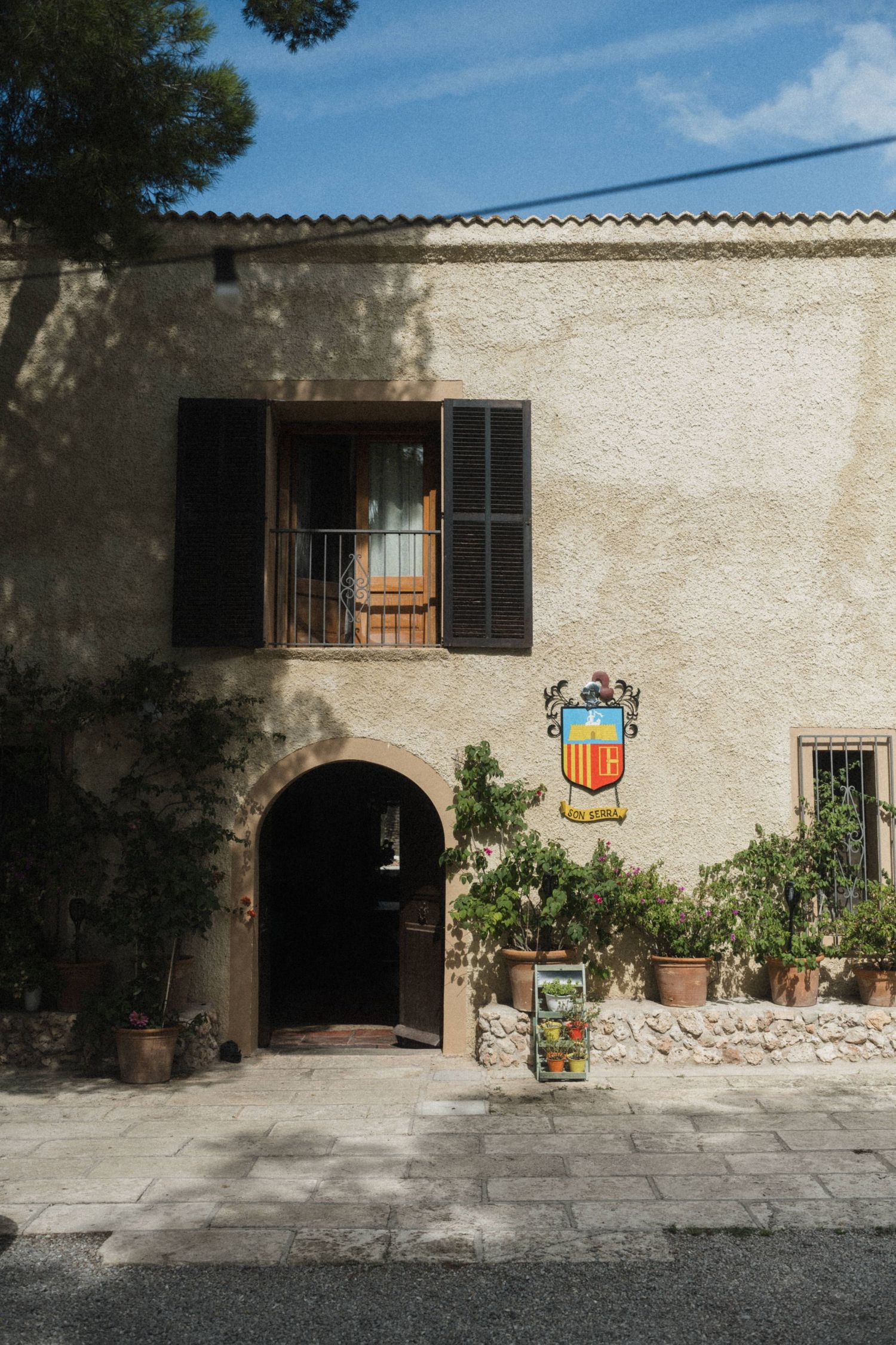 Rustic Mediterranean building facade with arched entrance, wooden shutters, and decorative coat of arms.