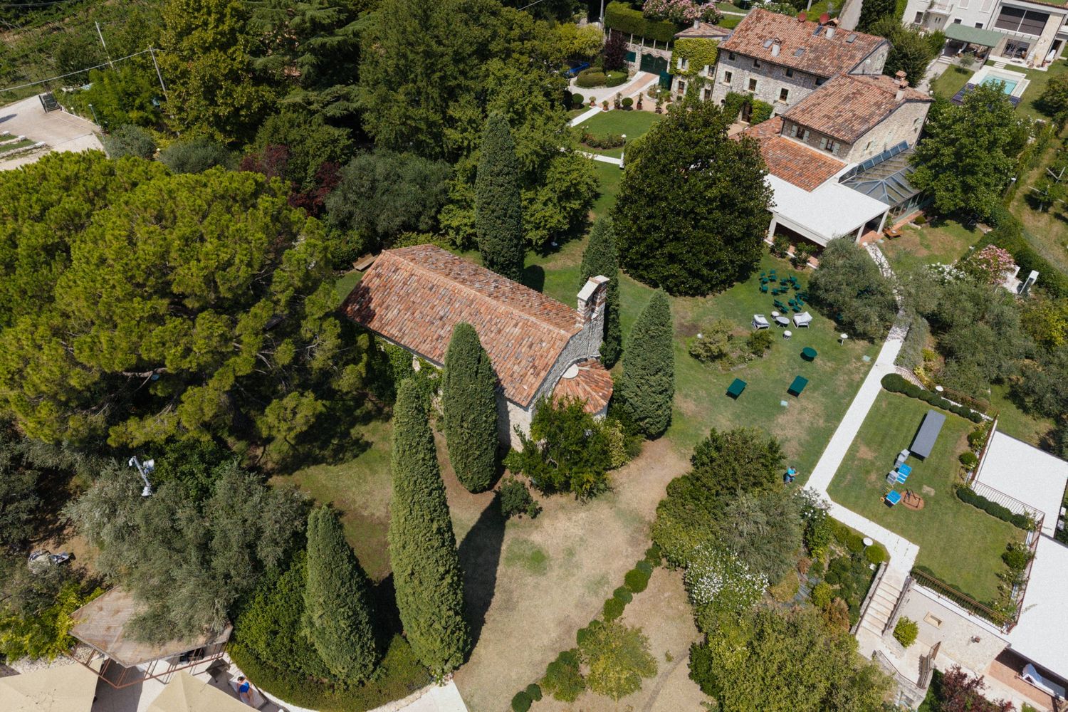 Aerial view of a Tuscan villa surrounded by lush cypress and pine trees with manicured gardens and terracotta rooftops.