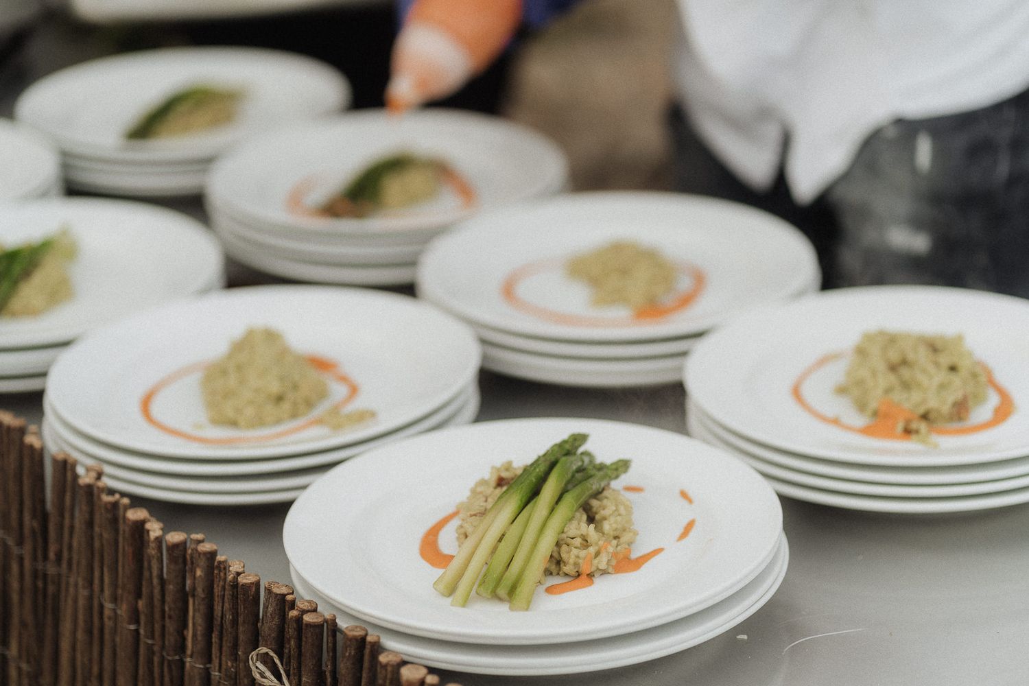 Elegant plated dishes with asparagus, grain salad, and orange sauce arranged on white plates at a catered outdoor event.