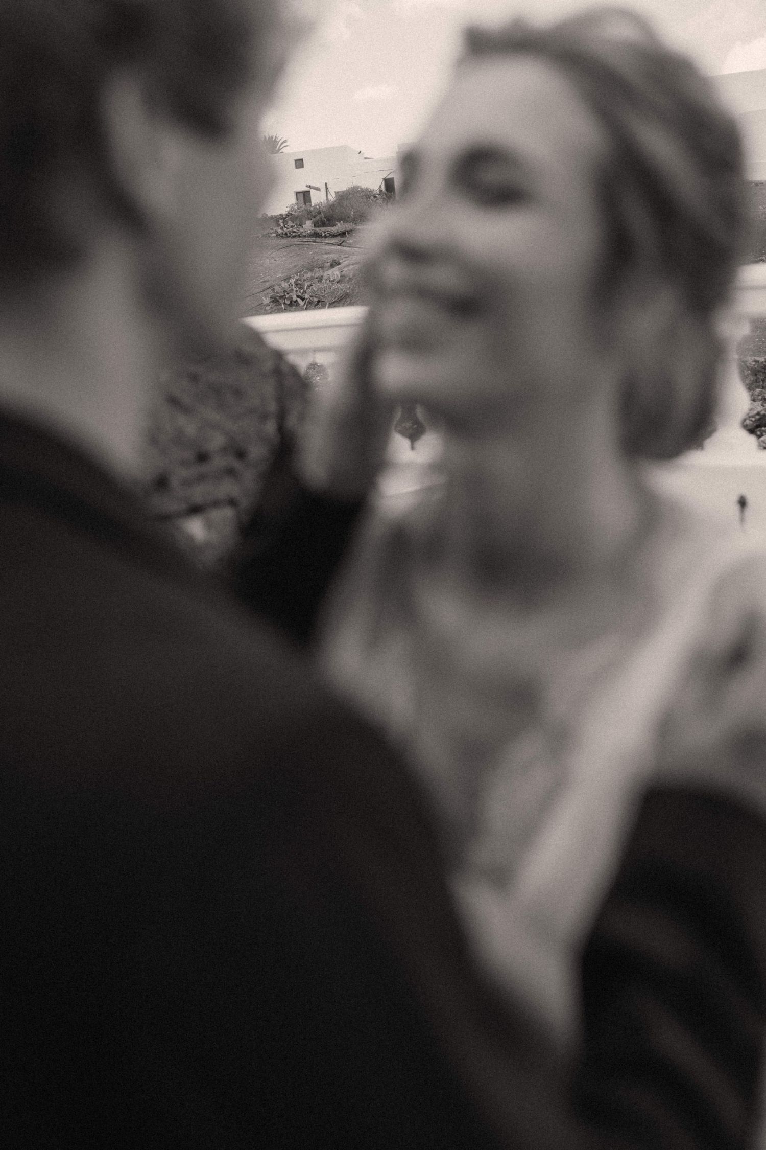 Black and white photo of a smiling bride and groom sharing a tender moment outdoors on their wedding day.