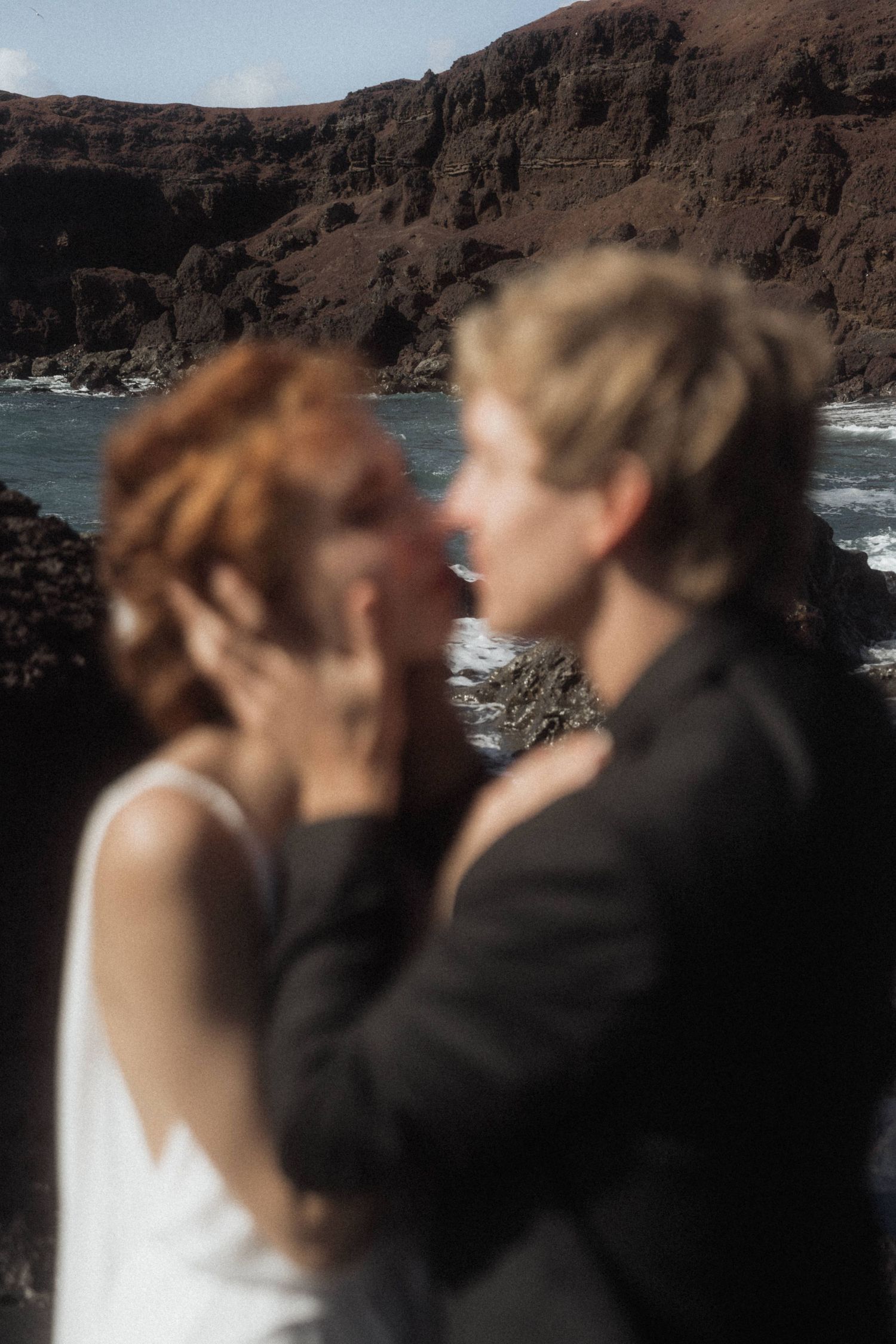 Couple sharing an intimate moment near rocky volcanic coastline during their beach elopement.