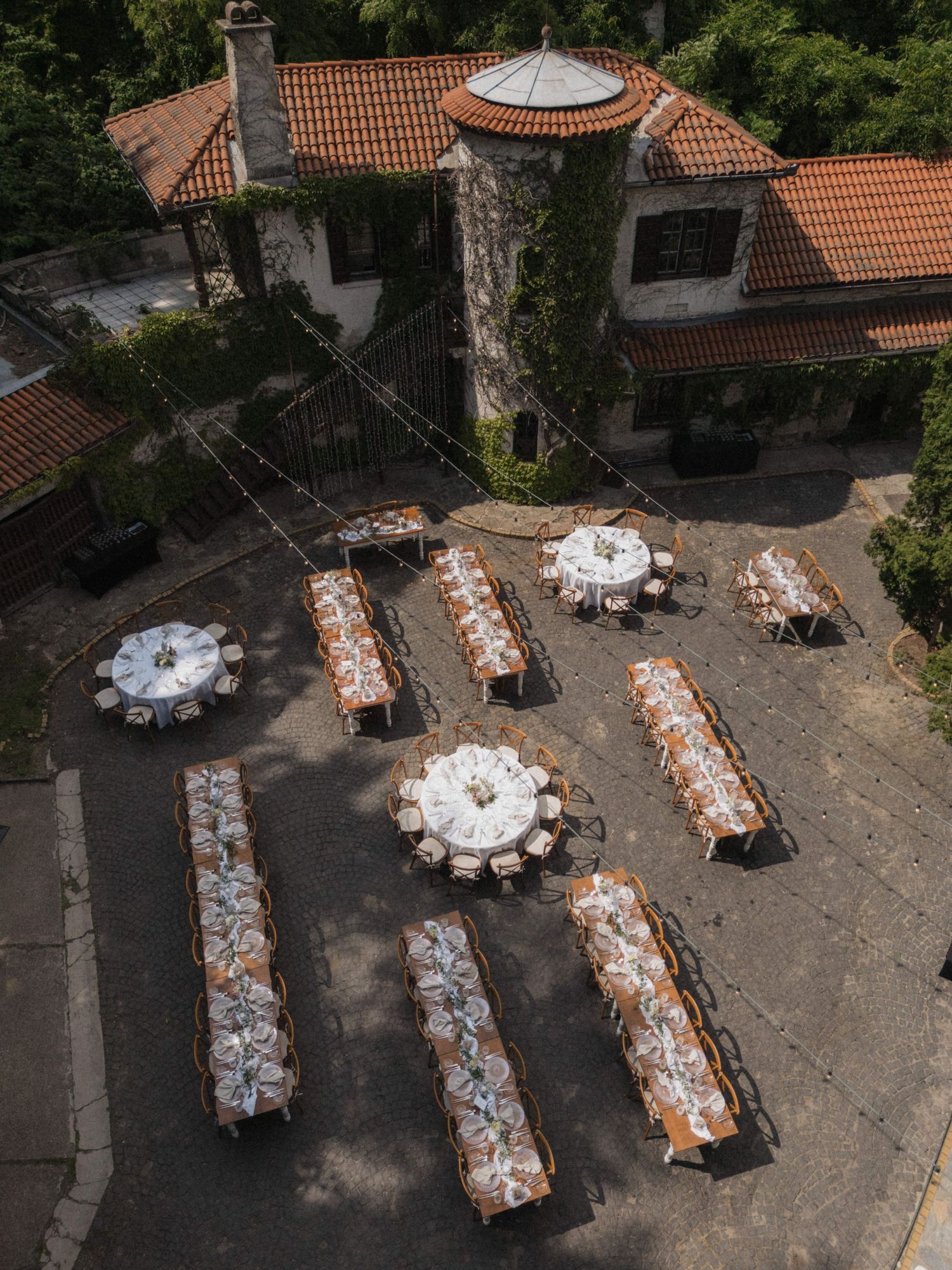 Aerial view of elegant outdoor wedding reception with round and rectangular tables at a villa.