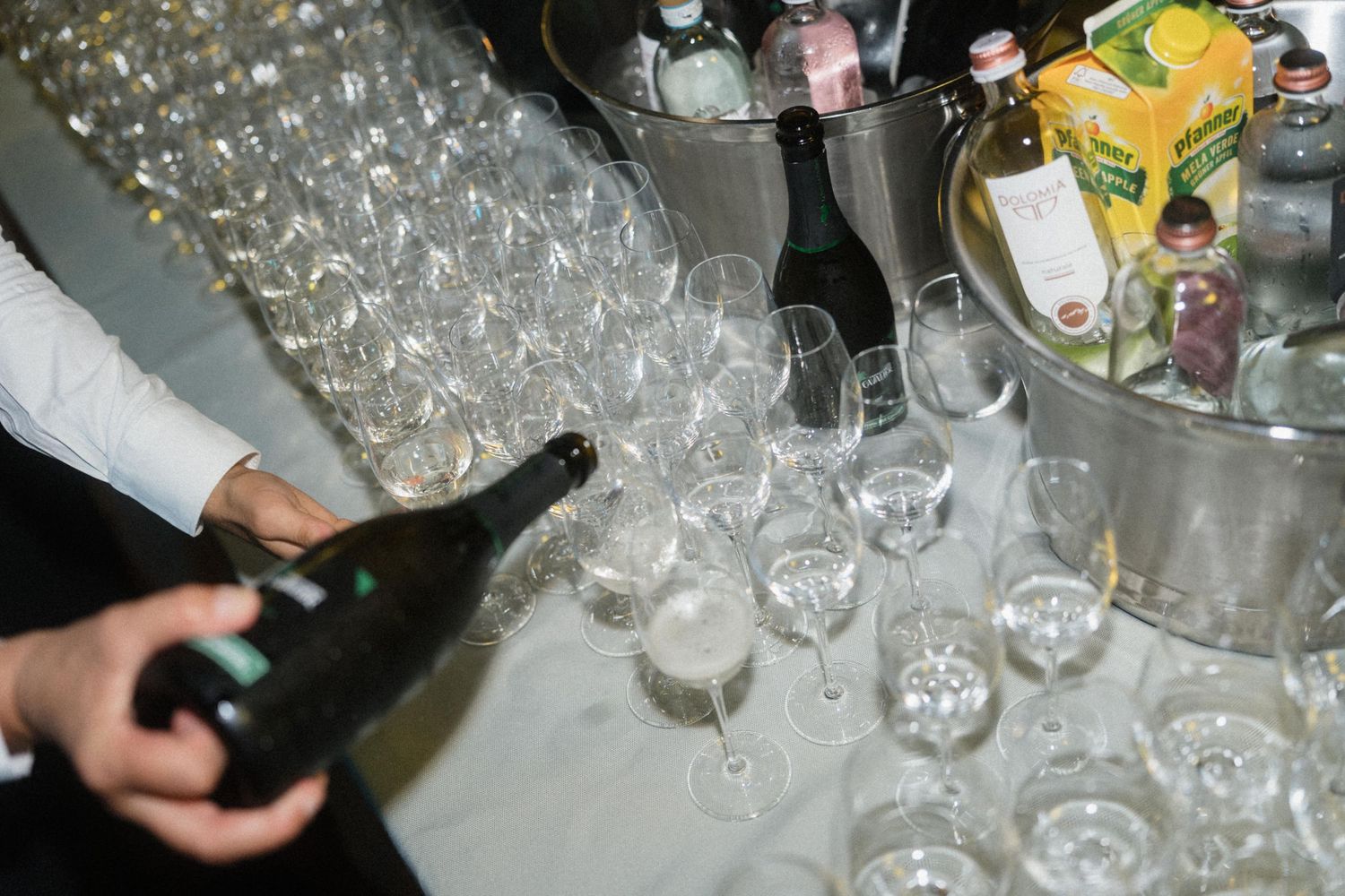 Bartender pouring champagne into elegant glasses at a festive event with bottles chilling in ice buckets.
