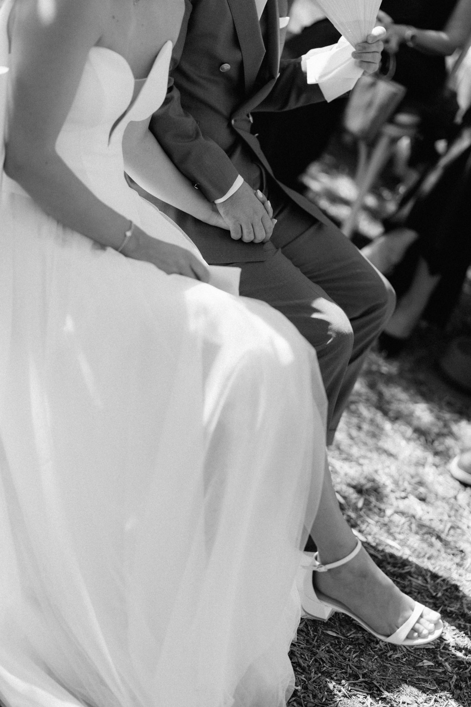 Black and white close-up of bride in white dress and groom holding hands during wedding ceremony.