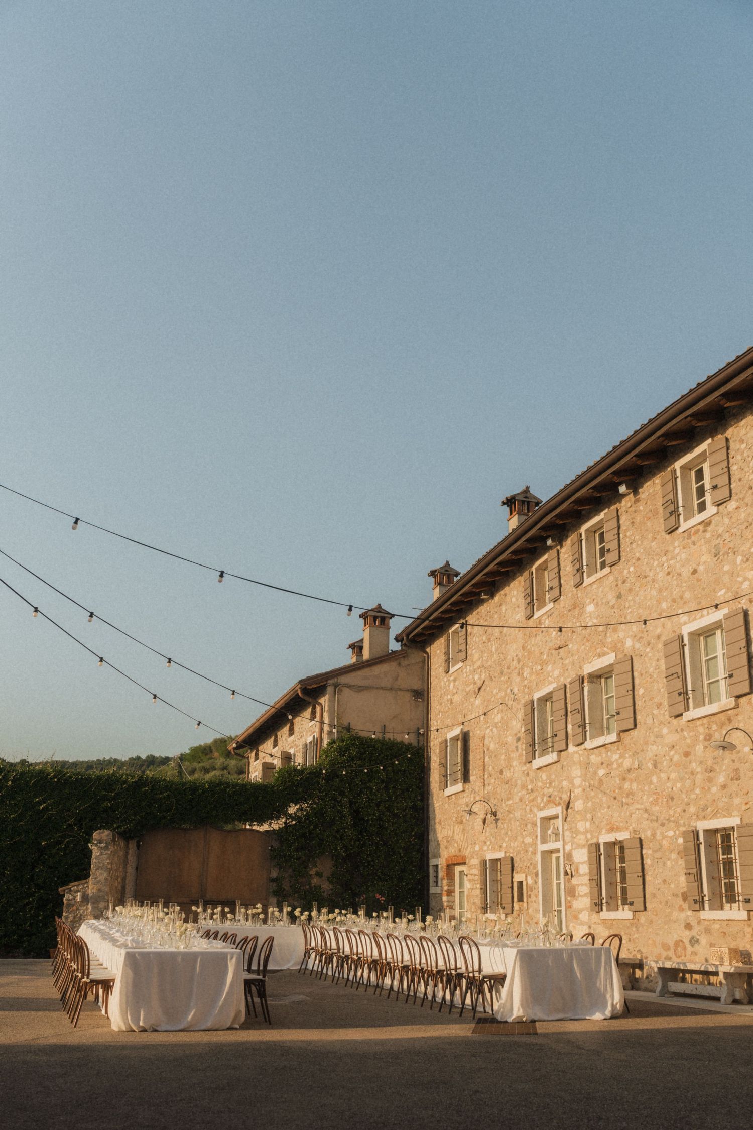 Elegant outdoor wedding reception tables set at golden hour beside rustic Italian stone villa.