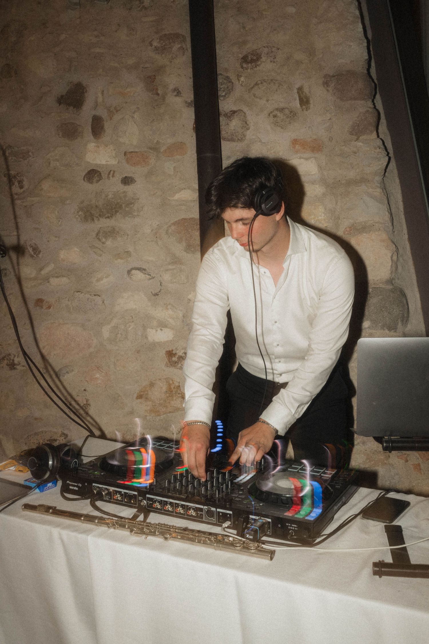 DJ in white shirt mixing music on turntables at rustic stone wall wedding venue.