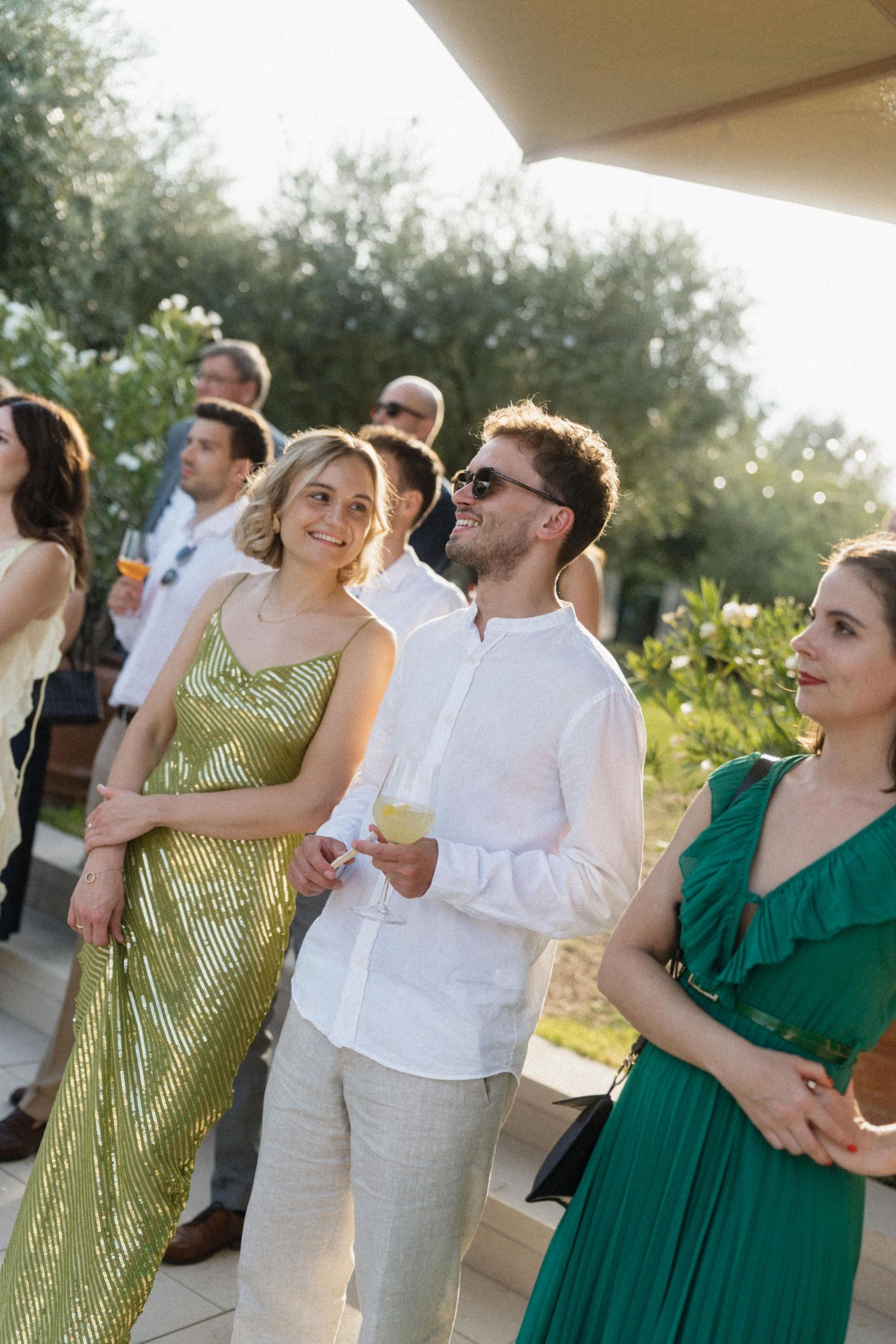 Elegantly dressed guests socializing outdoors at a summer wedding reception in a sunlit garden venue.