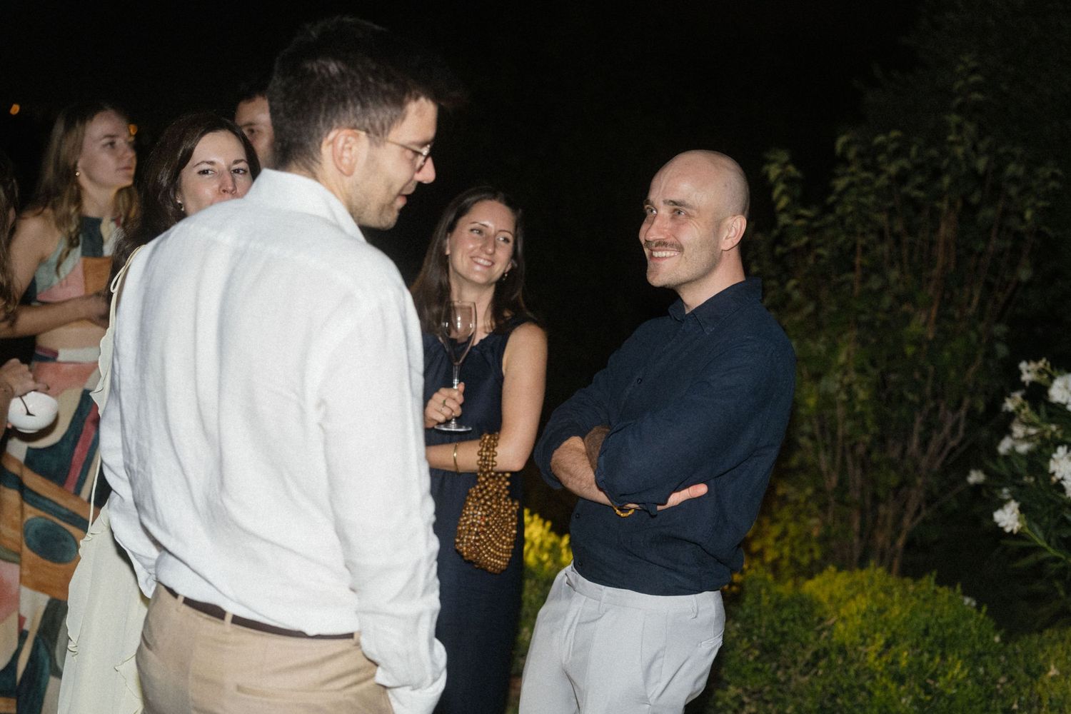 Wedding guests socializing and smiling outdoors at night during an elegant garden wedding reception.