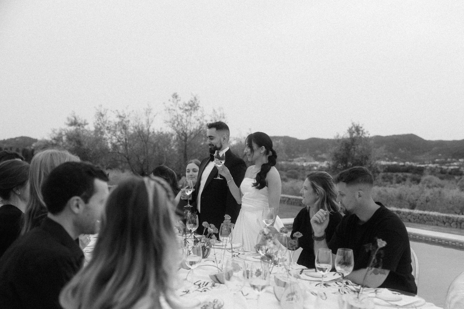 Bride and groom sharing a kiss at outdoor wedding reception dinner table in black and white.