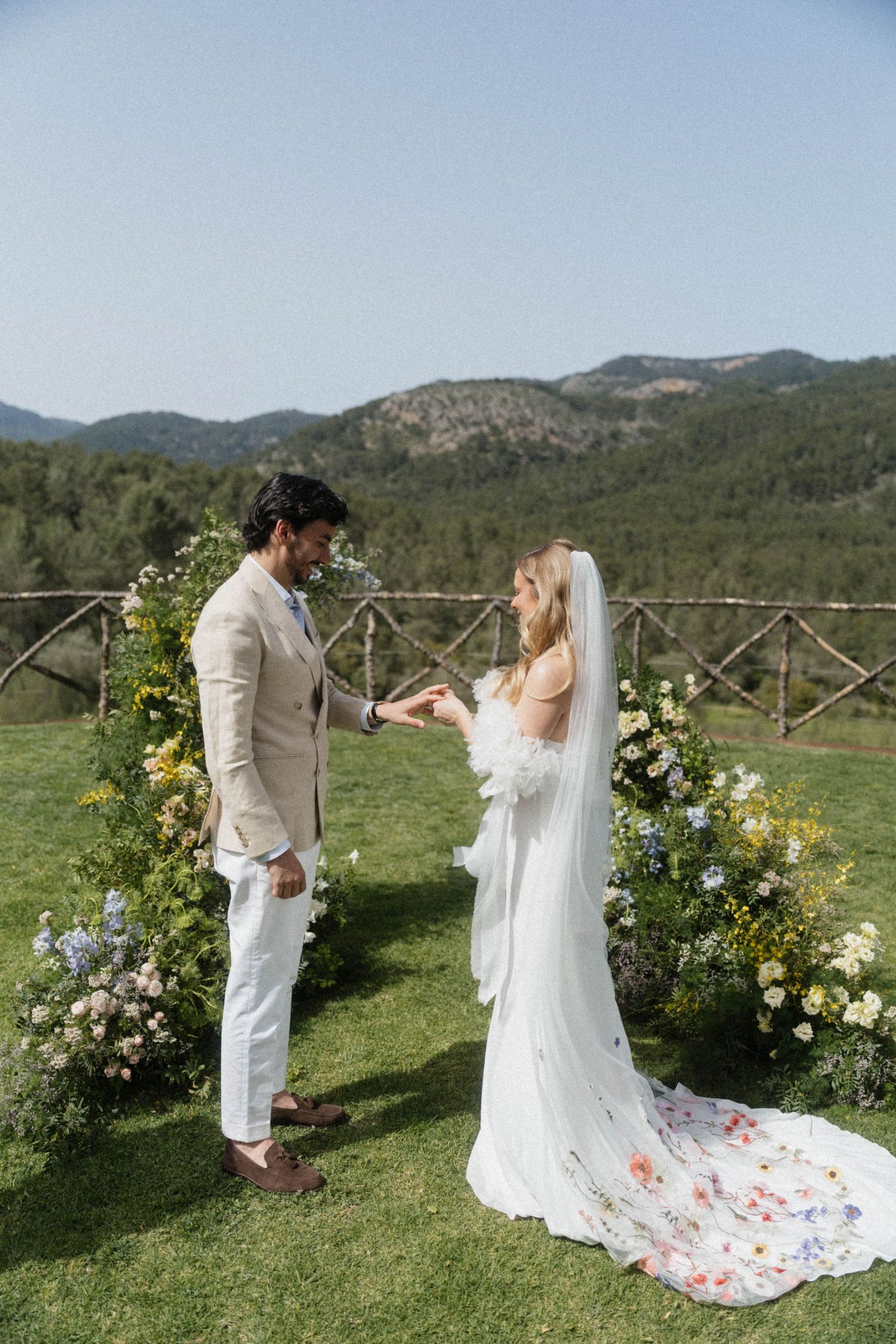 Bride and groom exchanging vows at a floral arch with mountain views at an outdoor wedding ceremony.