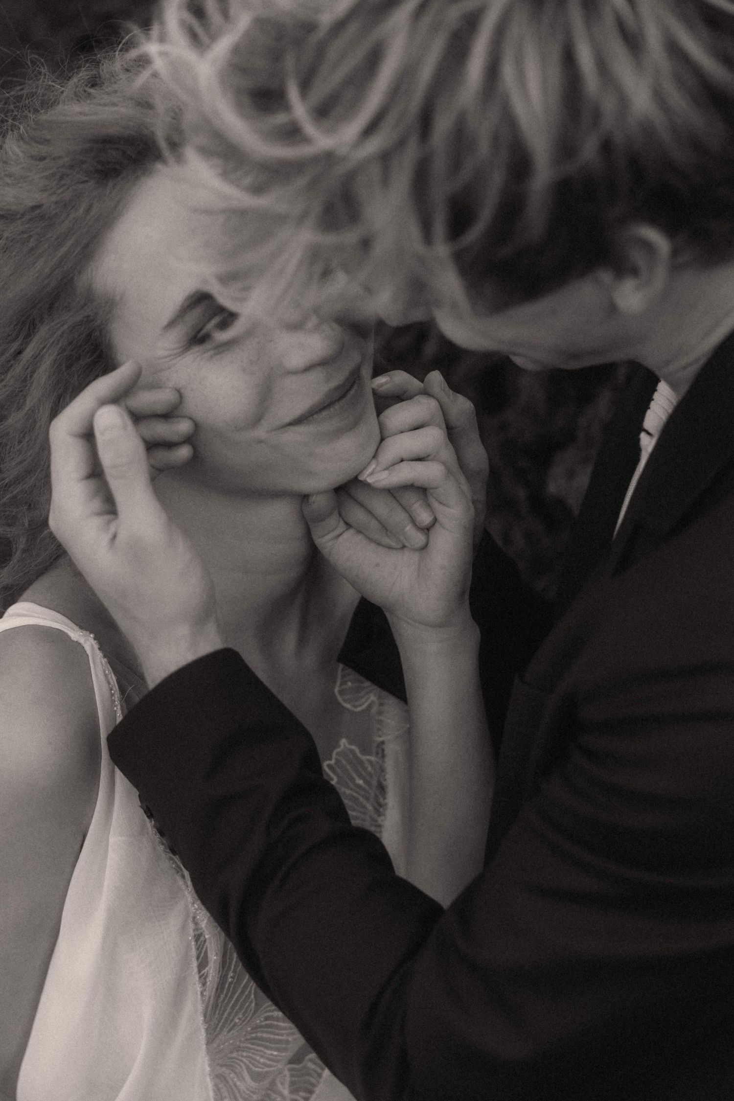 Black and white romantic portrait of groom tenderly cradling brides face during wedding celebration.