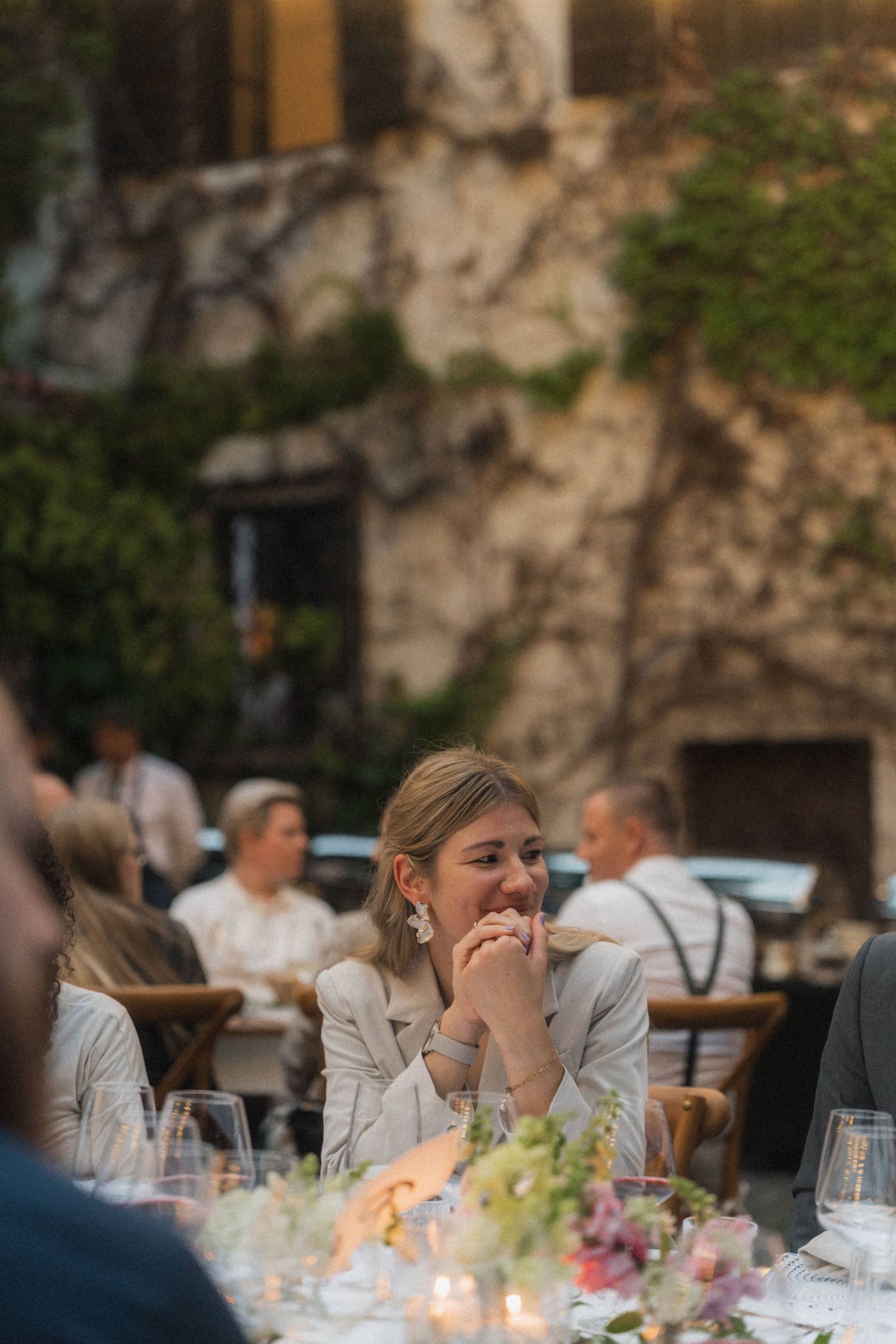 Emotional wedding guest laughs joyfully while seated at outdoor candlelit reception dinner table.