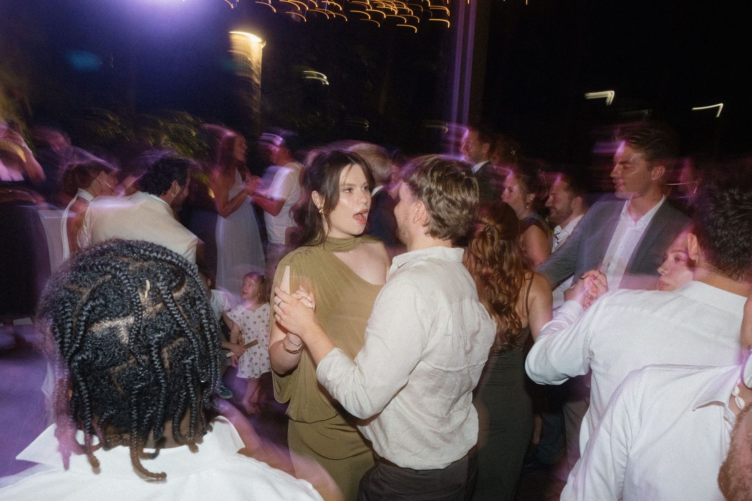 Couples dancing together at an outdoor wedding reception party at night.