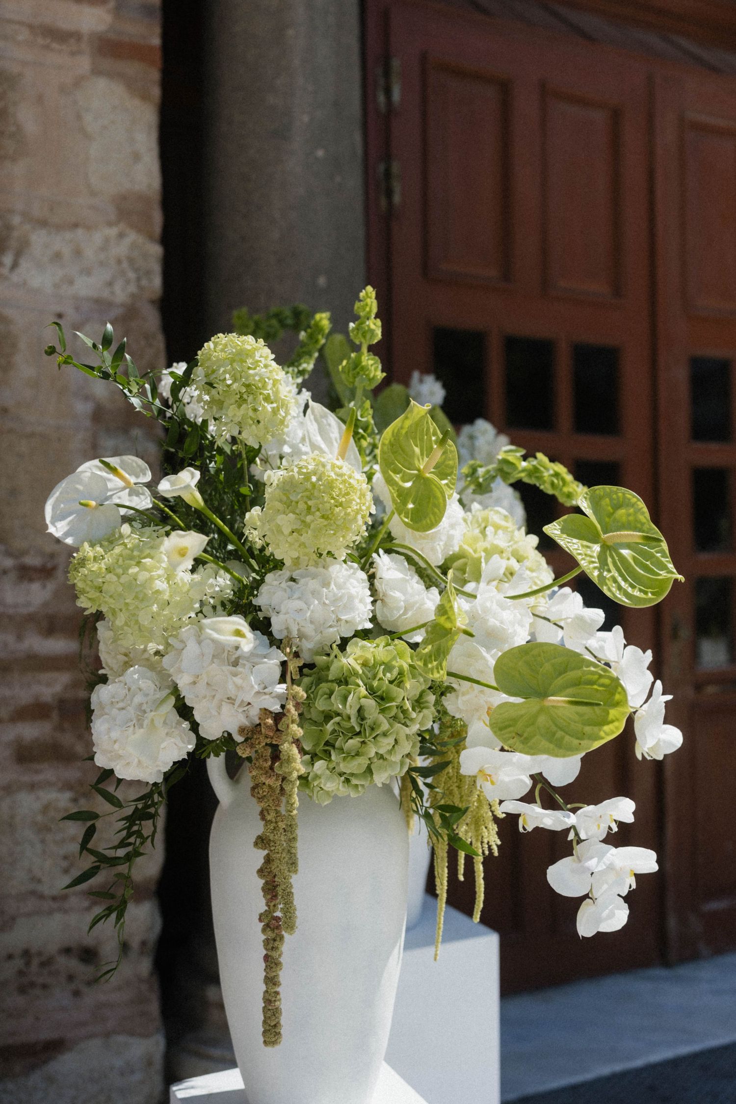Large white floral arrangement with hydrangeas and anthurium in white vase at church entrance.