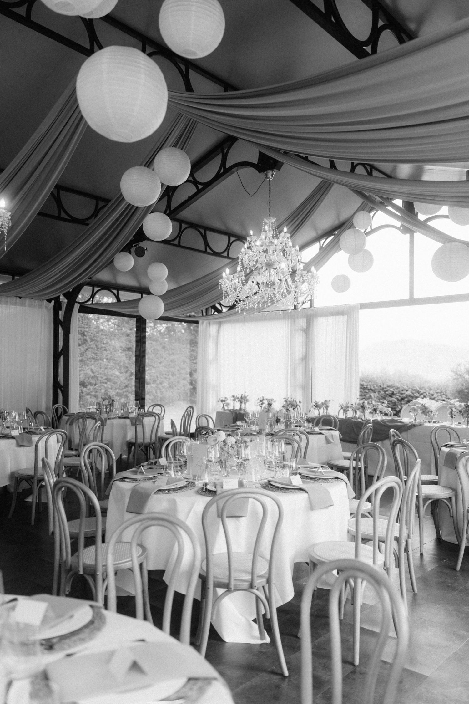 Elegant black and white wedding reception venue with round tables, Bentwood chairs, and paper lanterns.